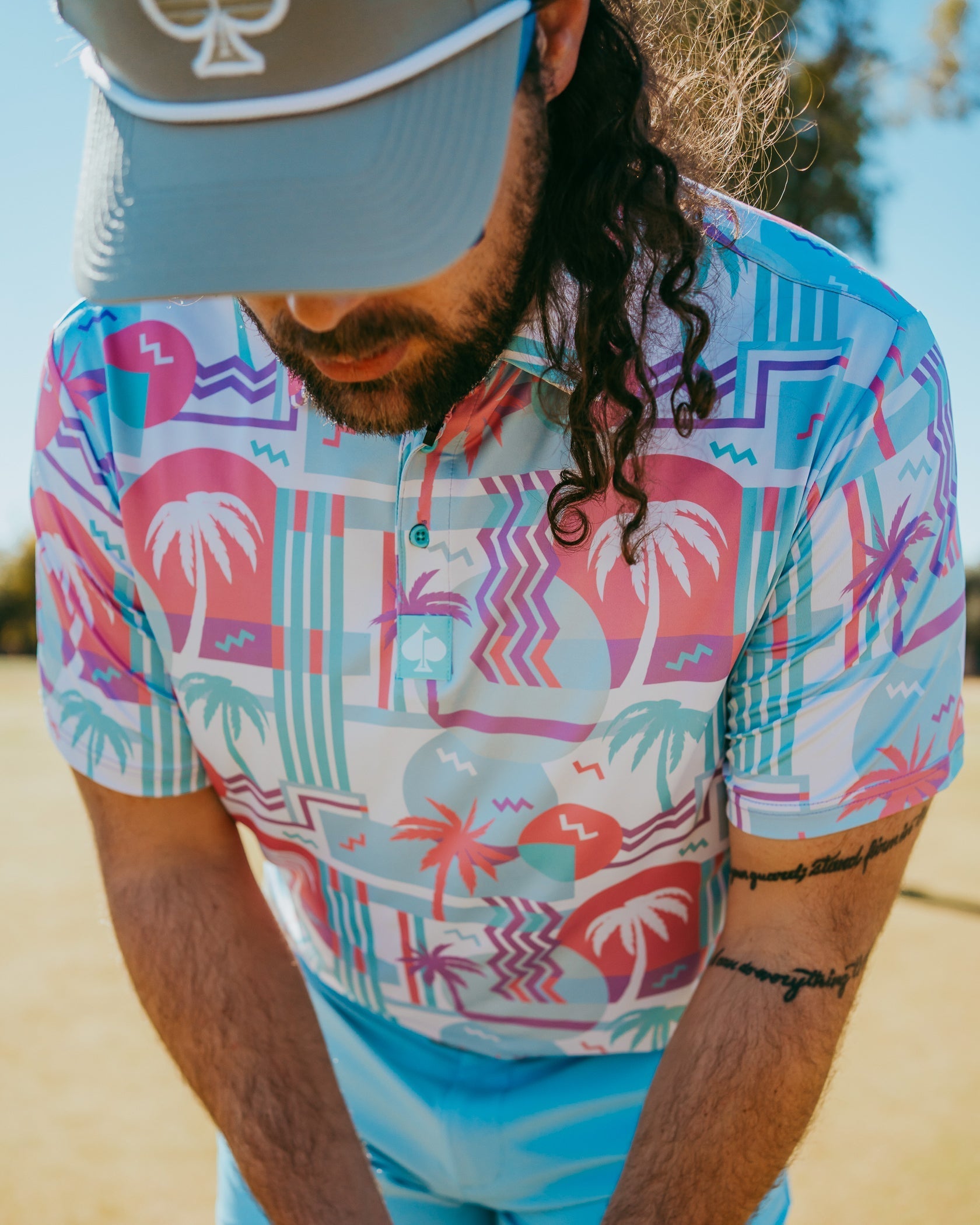 Colorful golf polo featuring a vibrant beach-themed pattern with palm trees and abstract shapes, perfect for summer play.