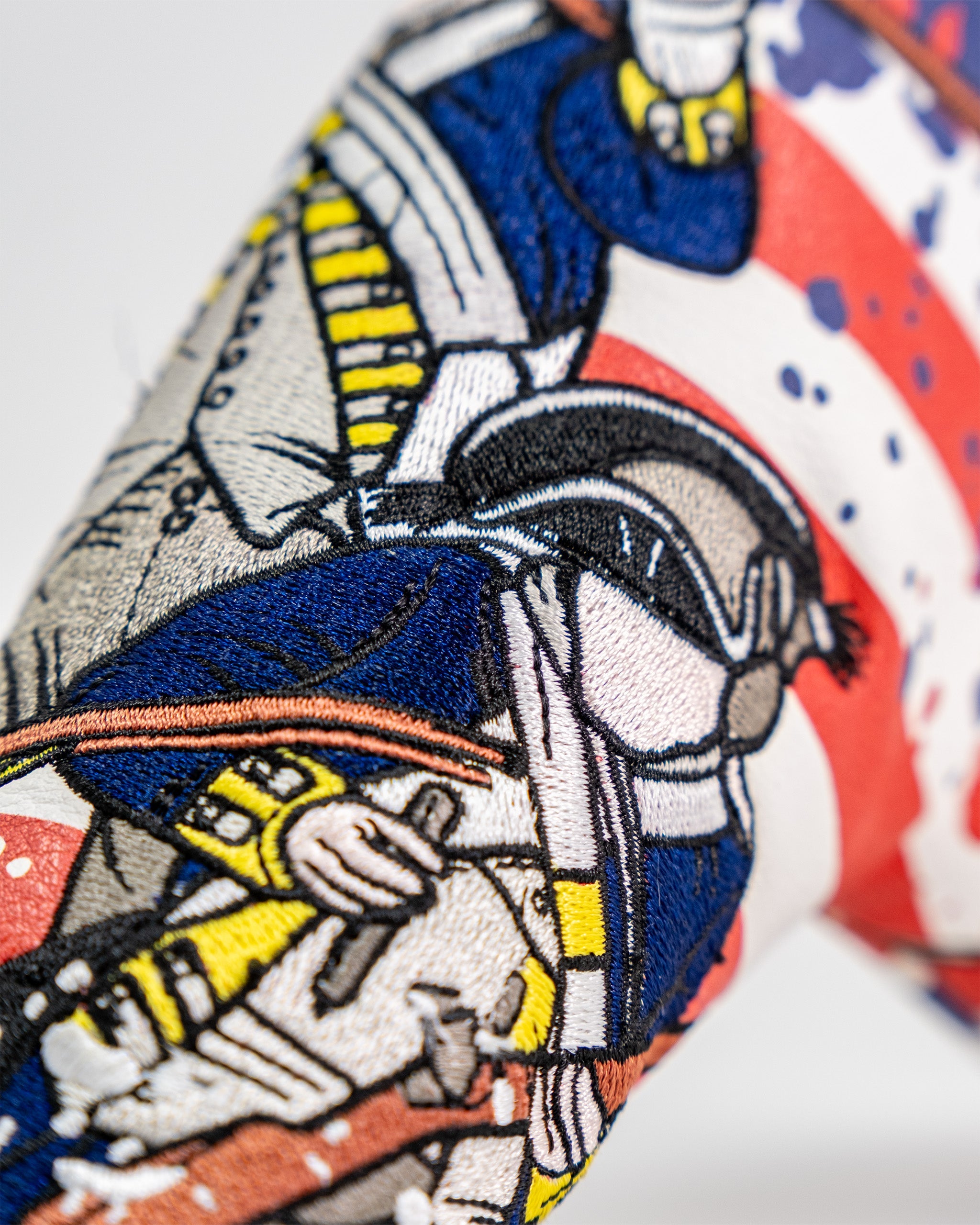 Embroidery of a colorful astronaut holding a tool, featuring detailed stitching on a golf blade putter cover.