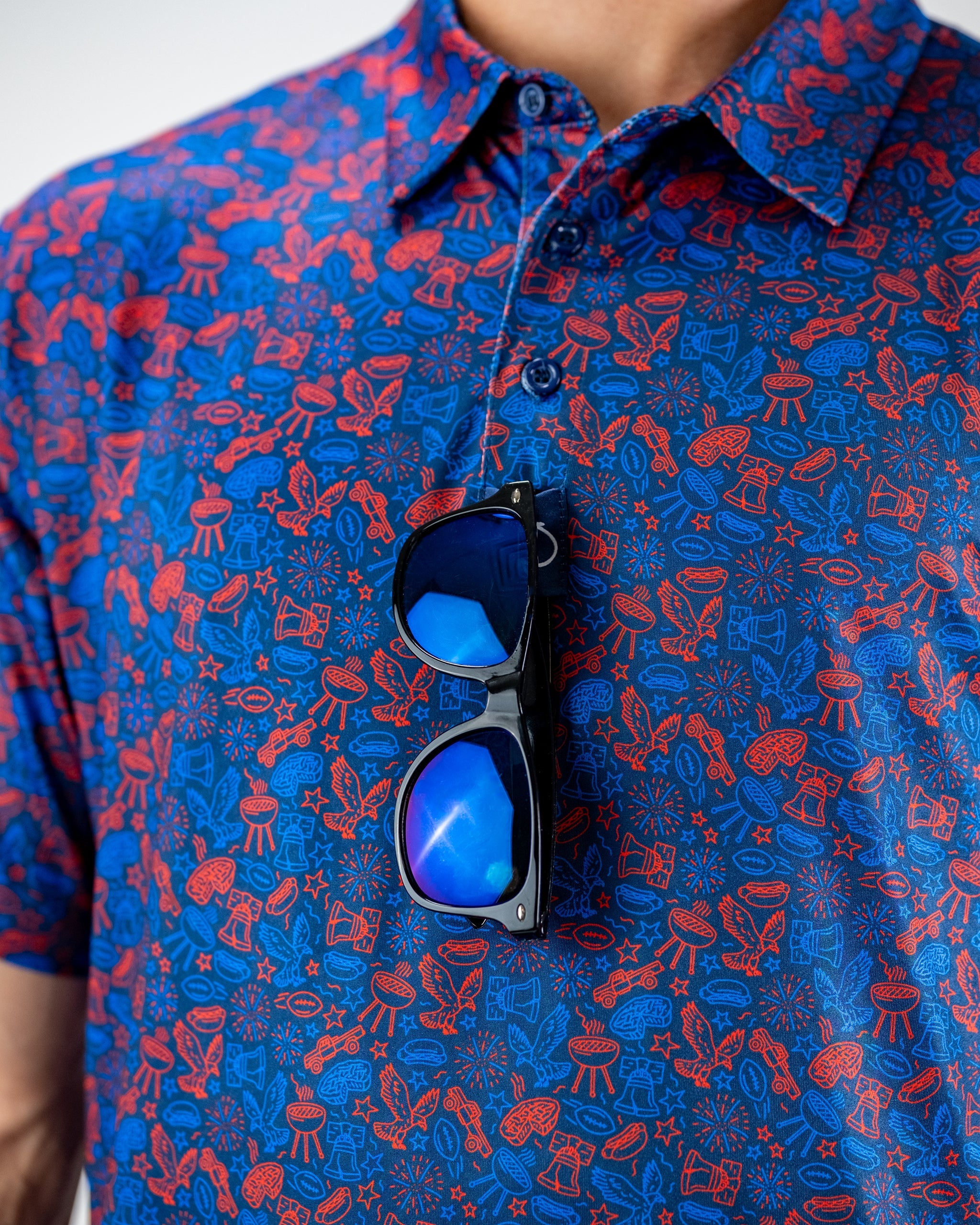 Navy polo shirt featuring a vibrant red and blue doodle pattern, with stylish sunglasses resting on the collar.