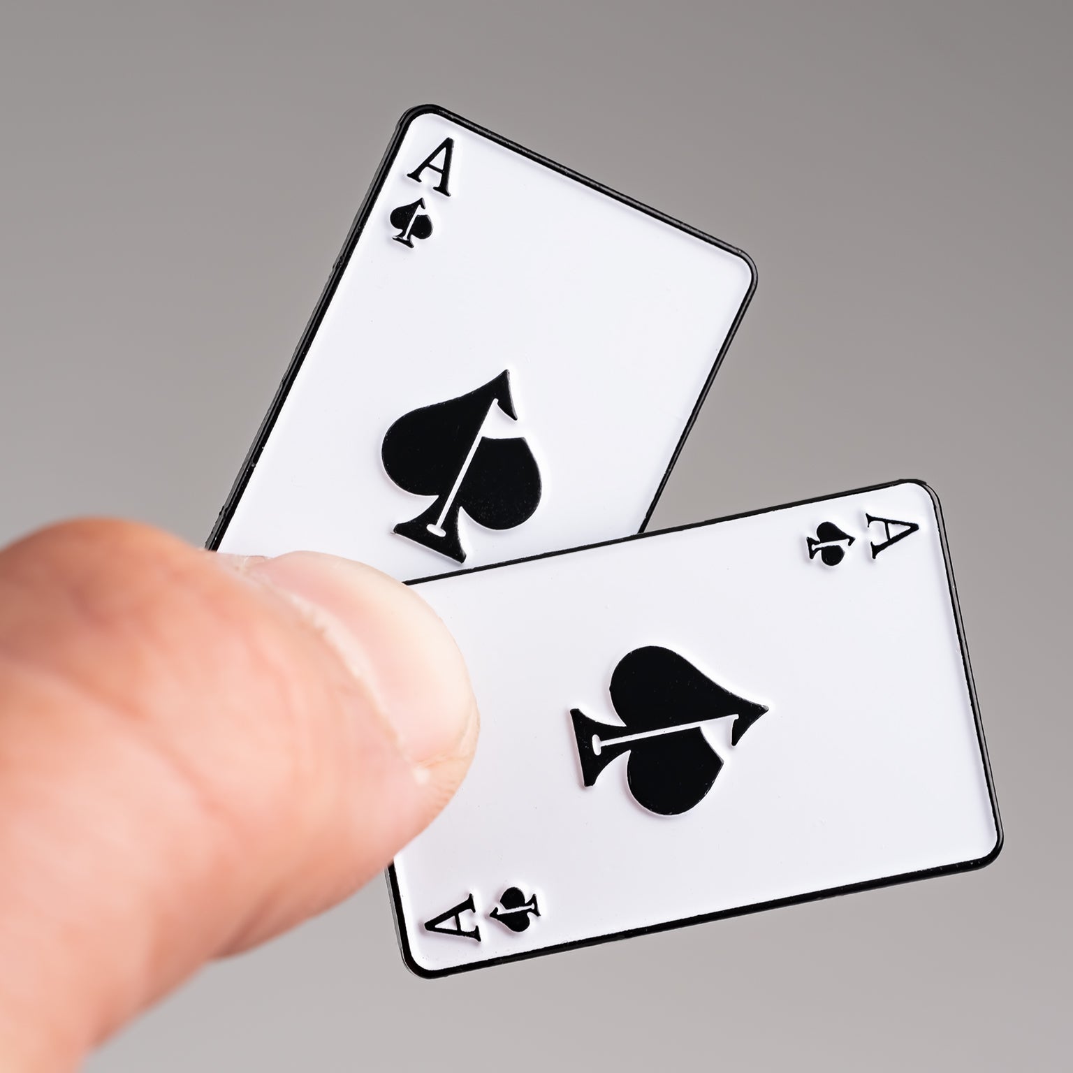 Alt text: "Close-up of a person holding an Ace of Spades ball marker, designed to resemble a playing card with a spade symbol, against a gray background."