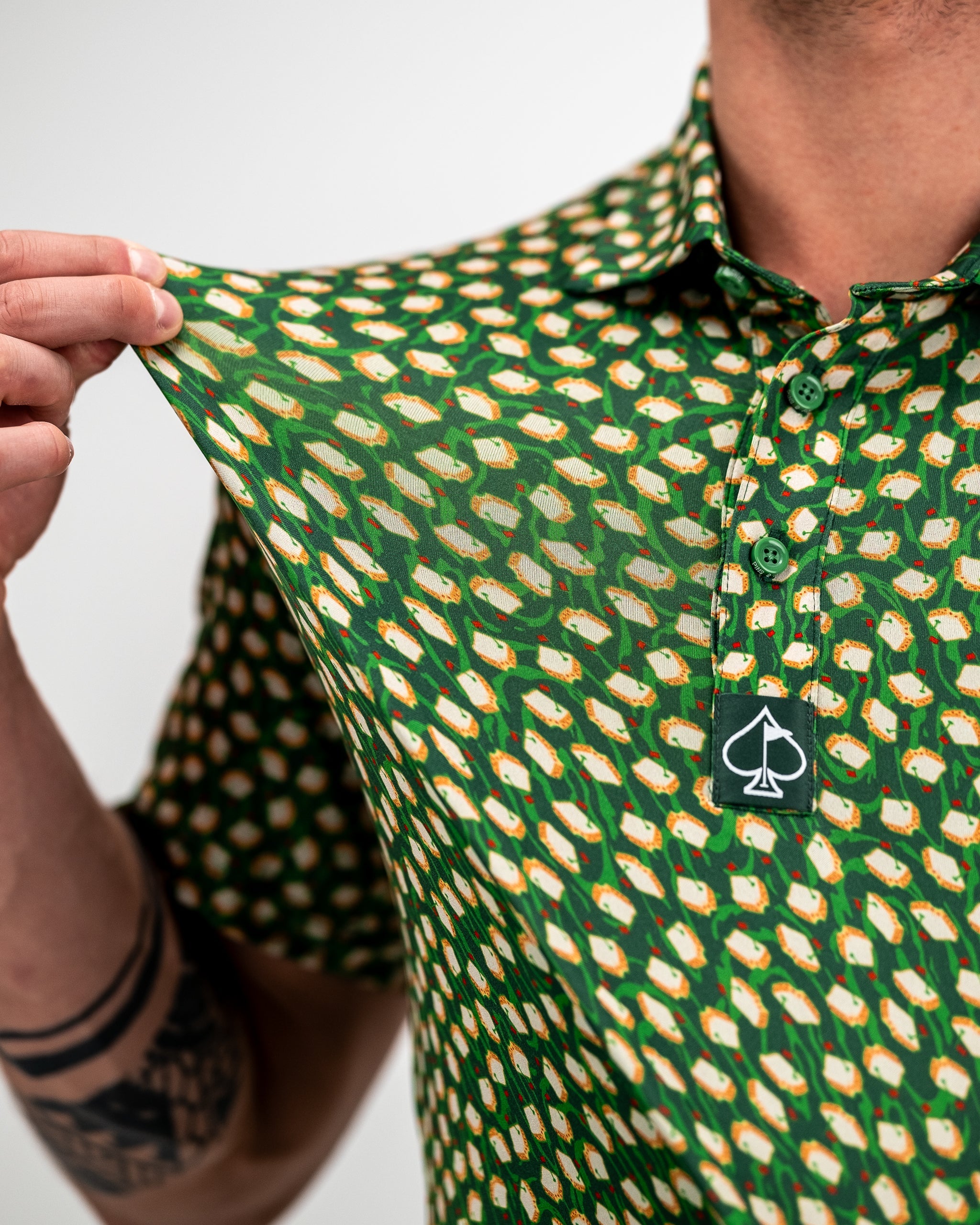 Close-up of a bold, green golf shirt with a colorful, abstract pattern featuring white, orange, and red accents; collar an...