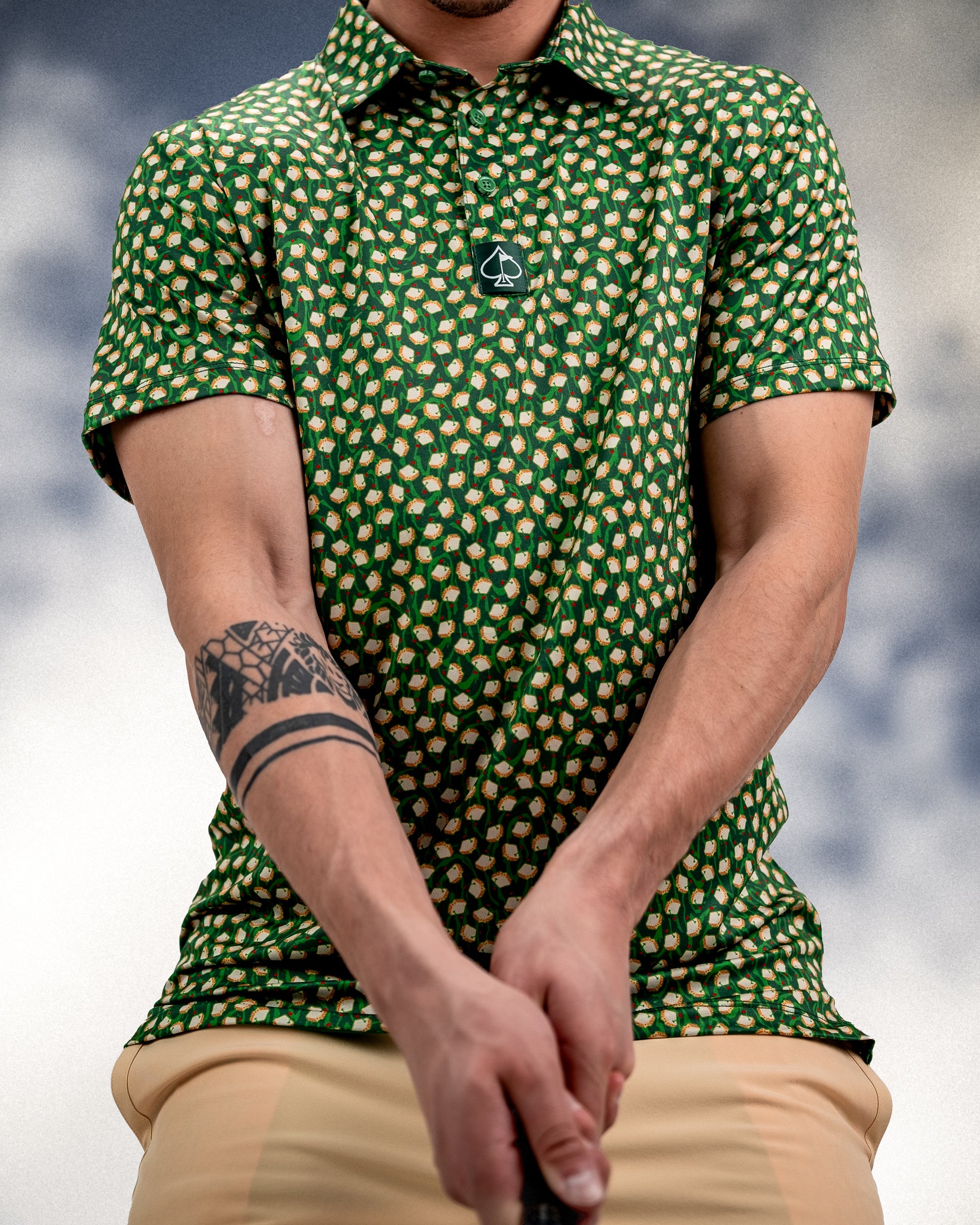 Green golf shirt with a bold pattern of golf balls, featuring a black and white spade logo on the chest.