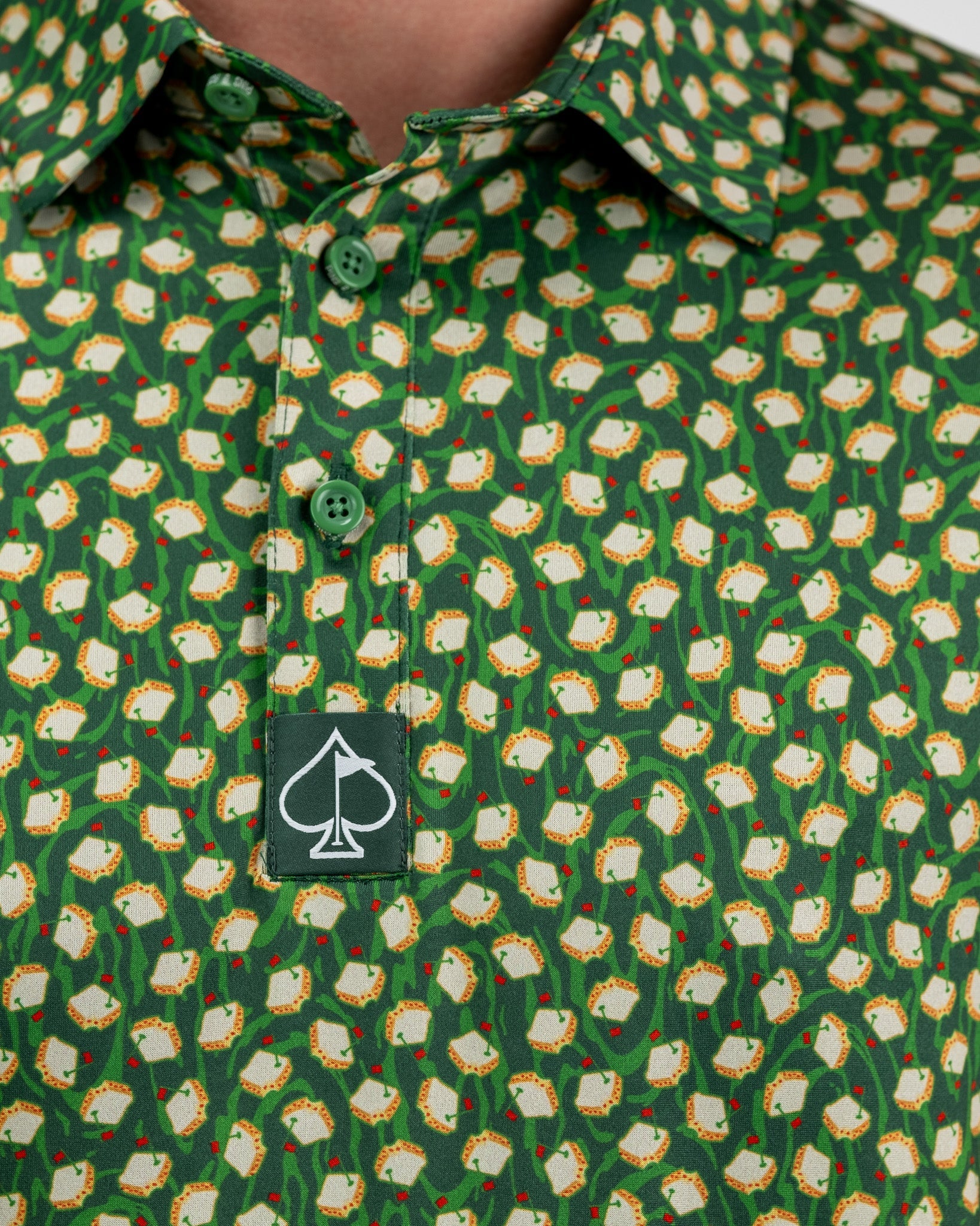 Green golf shirt with a playful toast and vine pattern, featuring green buttons and a black spade logo tag.