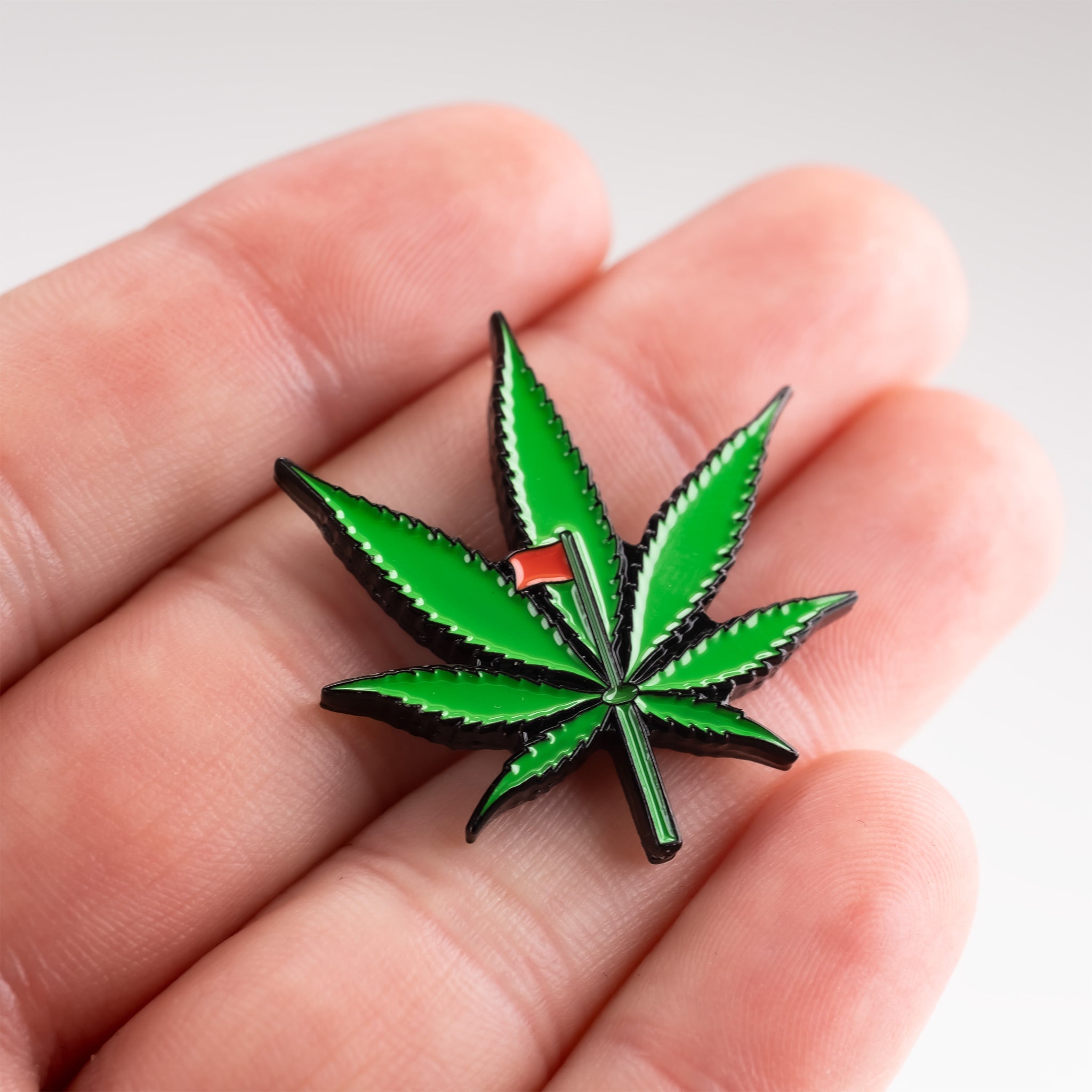 Pot leaf ball marker held in a hand, featuring a vibrant green design on a circular metal surface.