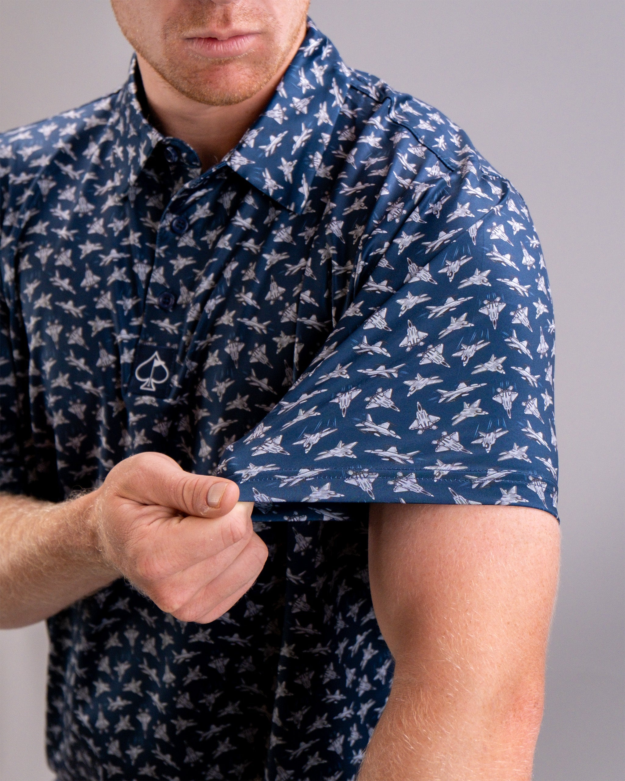 A person wearing a navy blue shirt with a white aircraft pattern, lifting the sleeve to reveal a "Birds of Steel" patch.