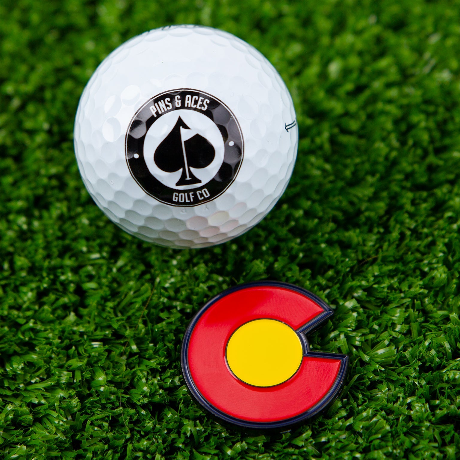 Colorado Strong ball marker featuring a circular design with the state flag colors of blue, yellow, and red, set against a grass background.
