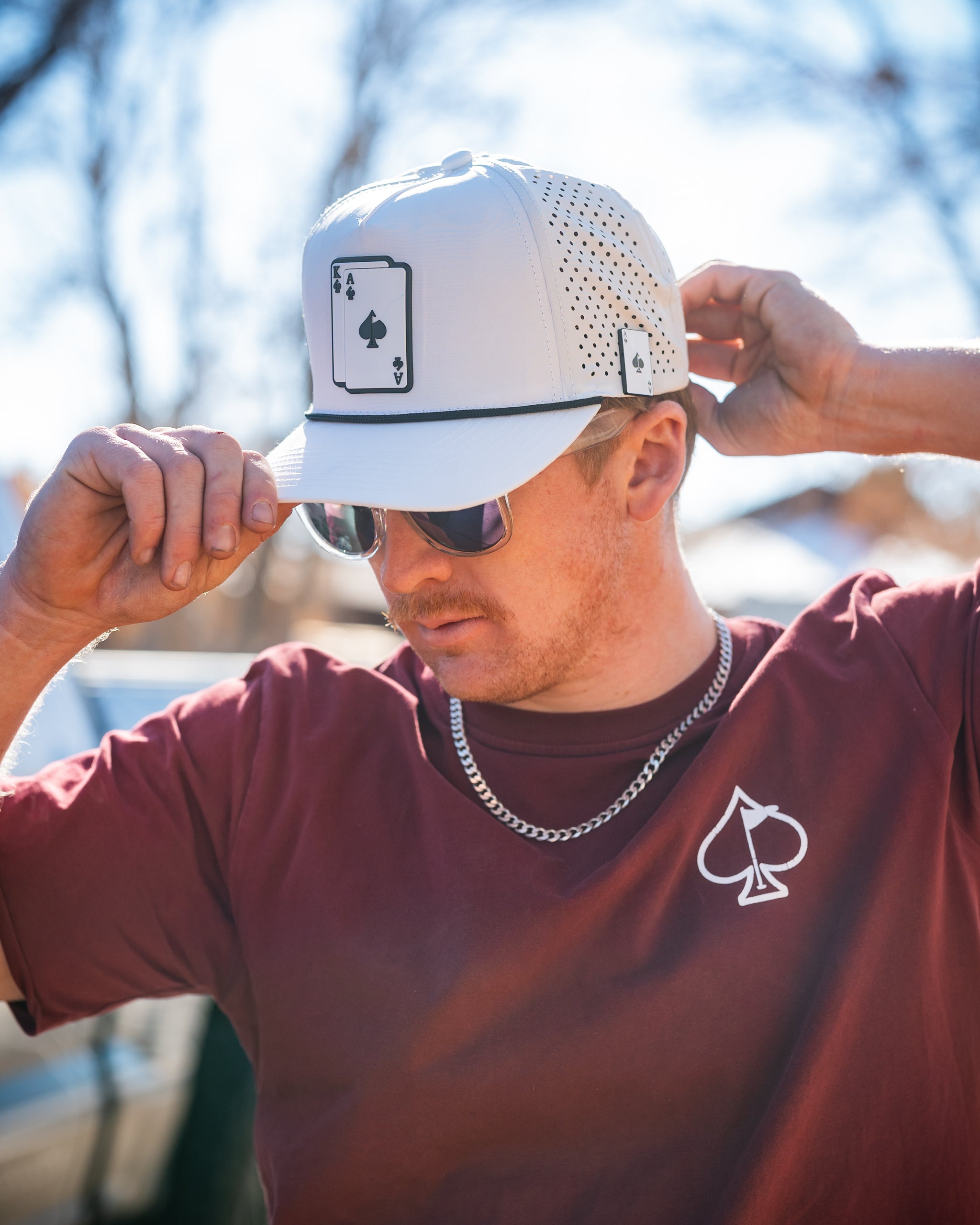 Perforated white rope hat with "AK" logo, featuring a stylish design and adjustable strap.