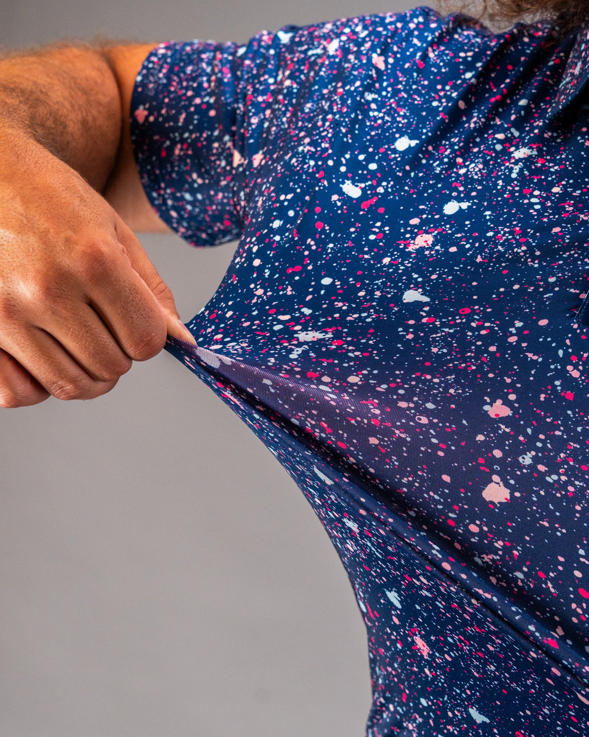 Bold blue splatter golf shirt featuring vibrant splashes of pink and white, showcasing its stretchy fabric and unique design.