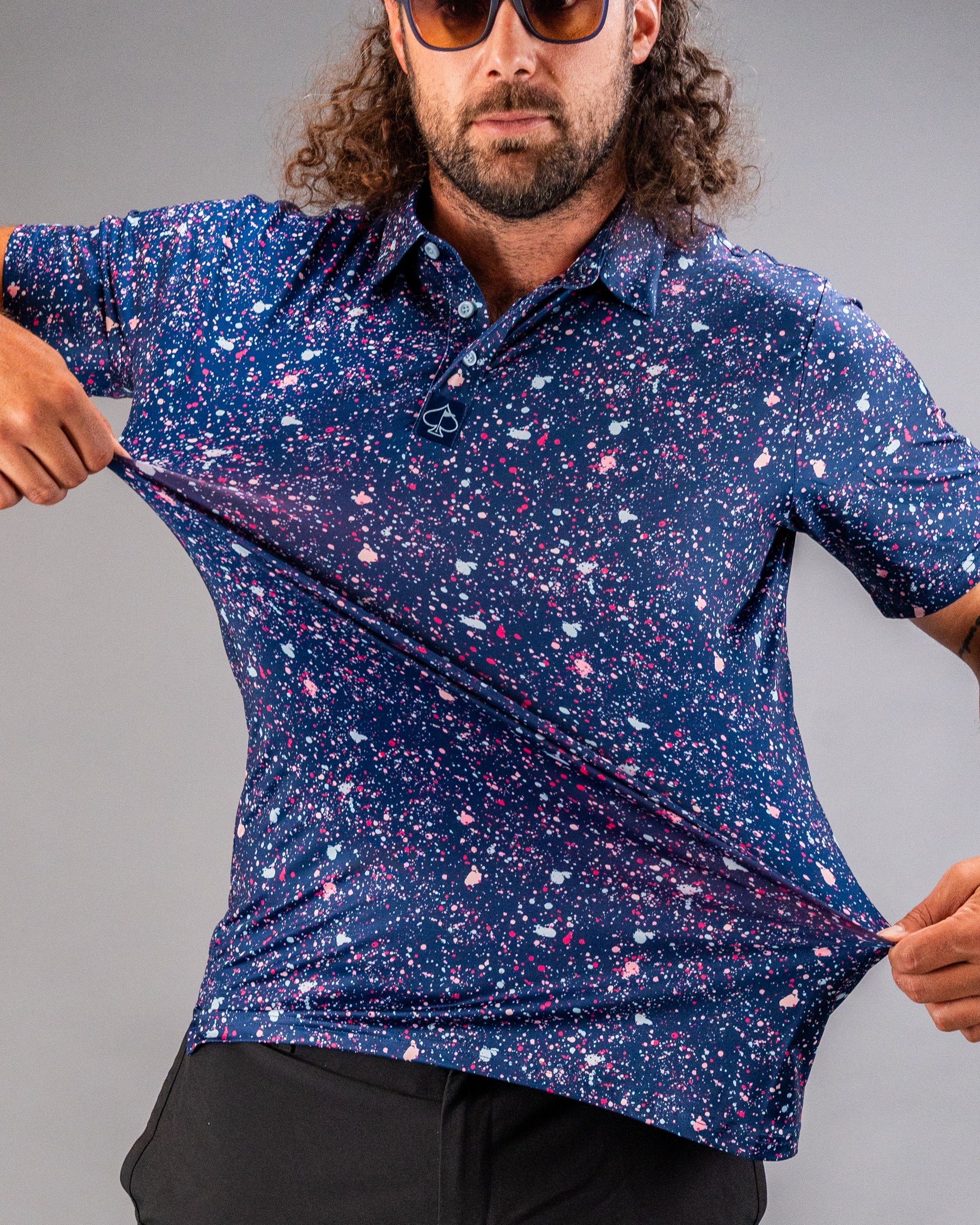A man in sunglasses showcases a blue splatter golf polo shirt, highlighting its vibrant, colorful design.