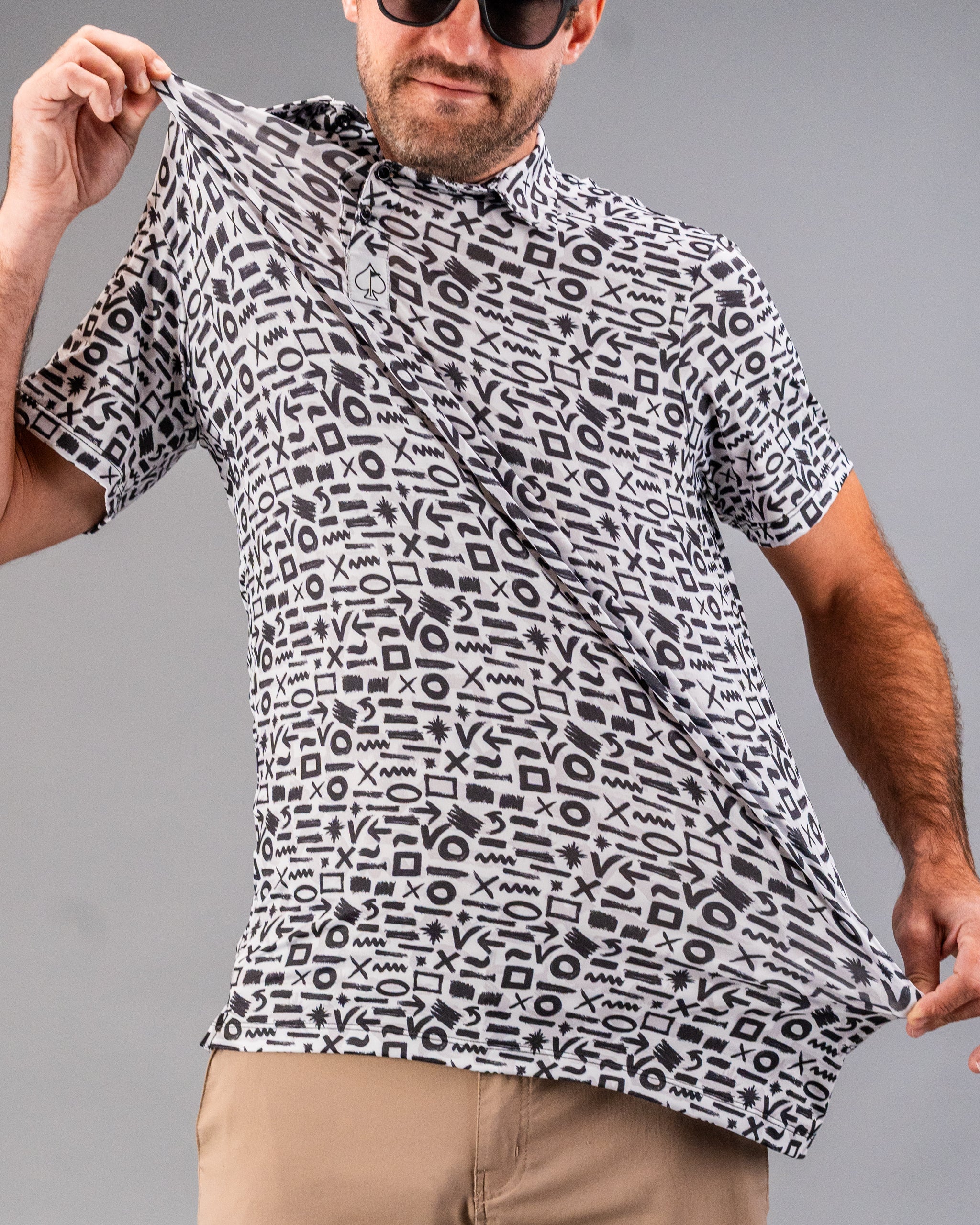 Man wearing a bold black and white geometric patterned golf shirt with short sleeves and beige shorts.