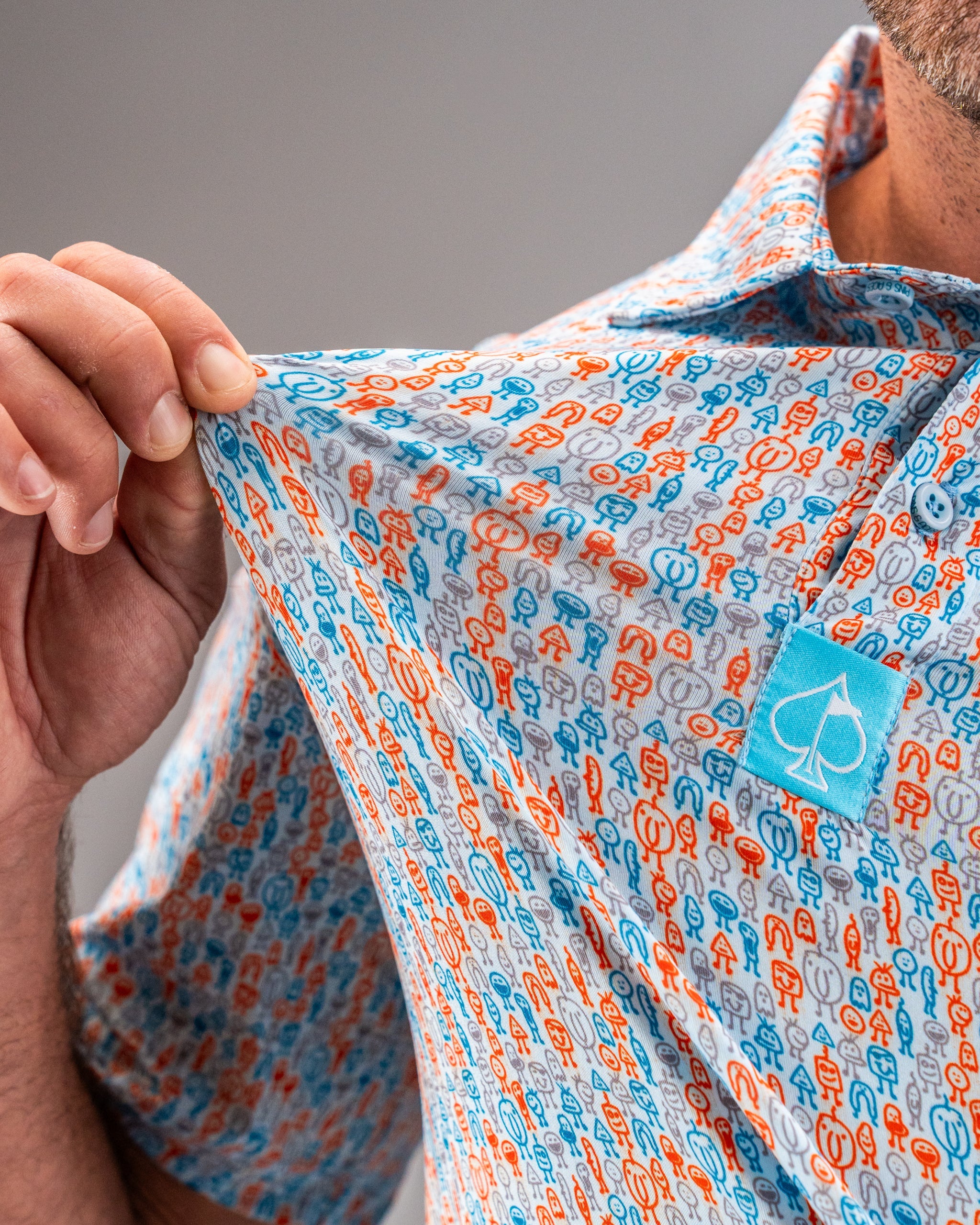 Close-up of a men's colorful golf shirt with a playful pattern in orange, blue, gray, and white, featuring small golf-them...