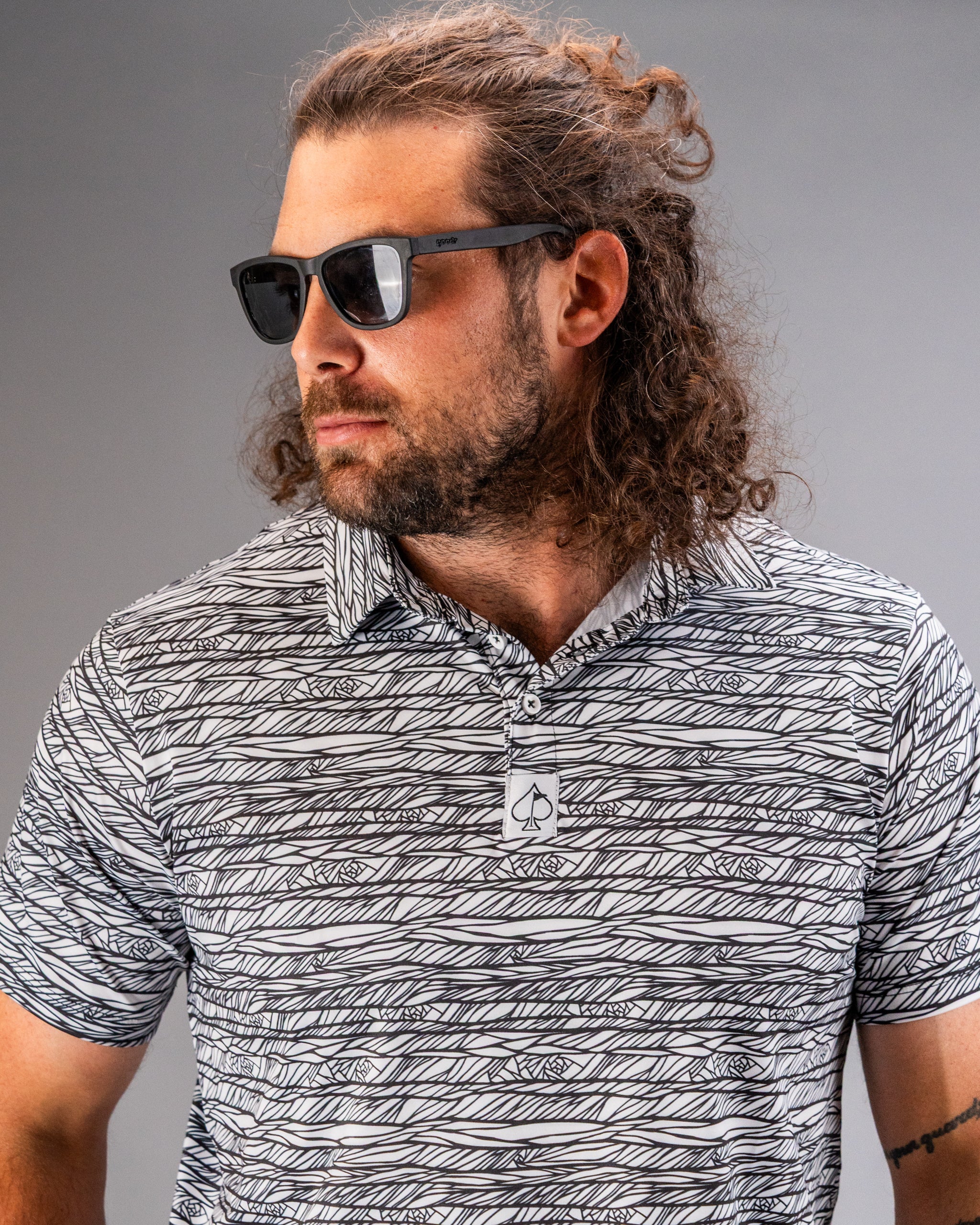 Stylish man wearing a black and white patterned golf polo with sunglasses, showcasing bold golf apparel.