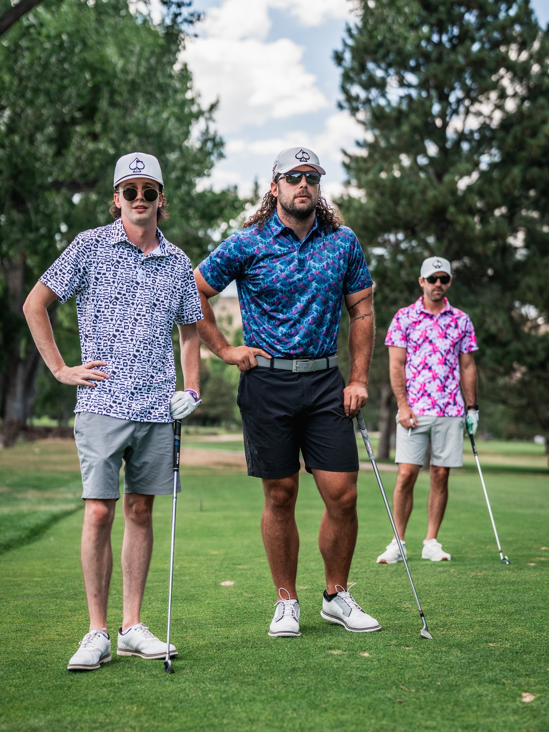 Three golfers in colorful, bold patterned shirts and hats, holding clubs on a lush golf course.