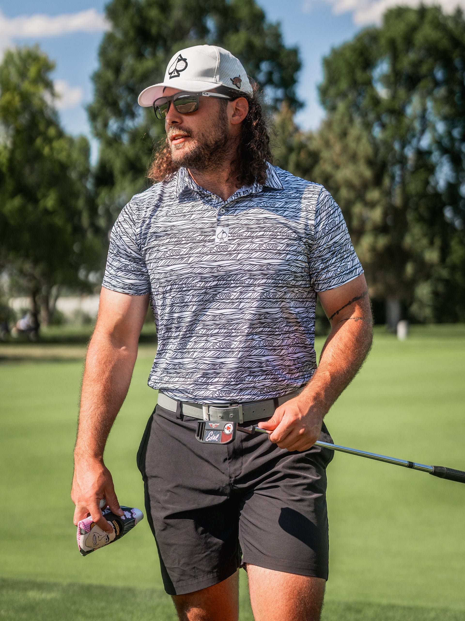Stylish golfer wearing a Fragment Black polo shirt and cap, holding a golf club on a sunny course.