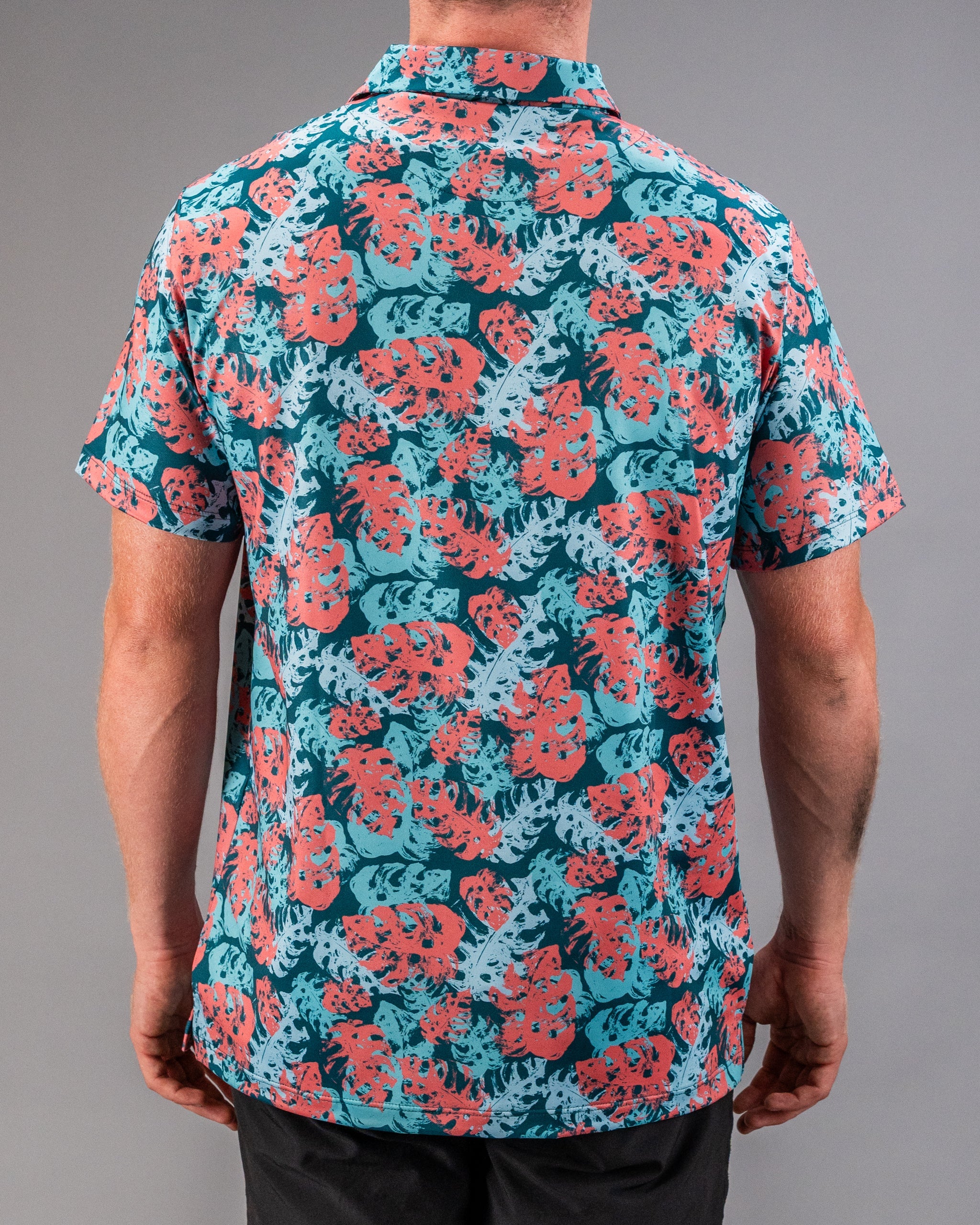 Men's tropical print golf shirt with red and blue leaf pattern, short sleeves, and relaxed fit. Perfect for bold golf style.
