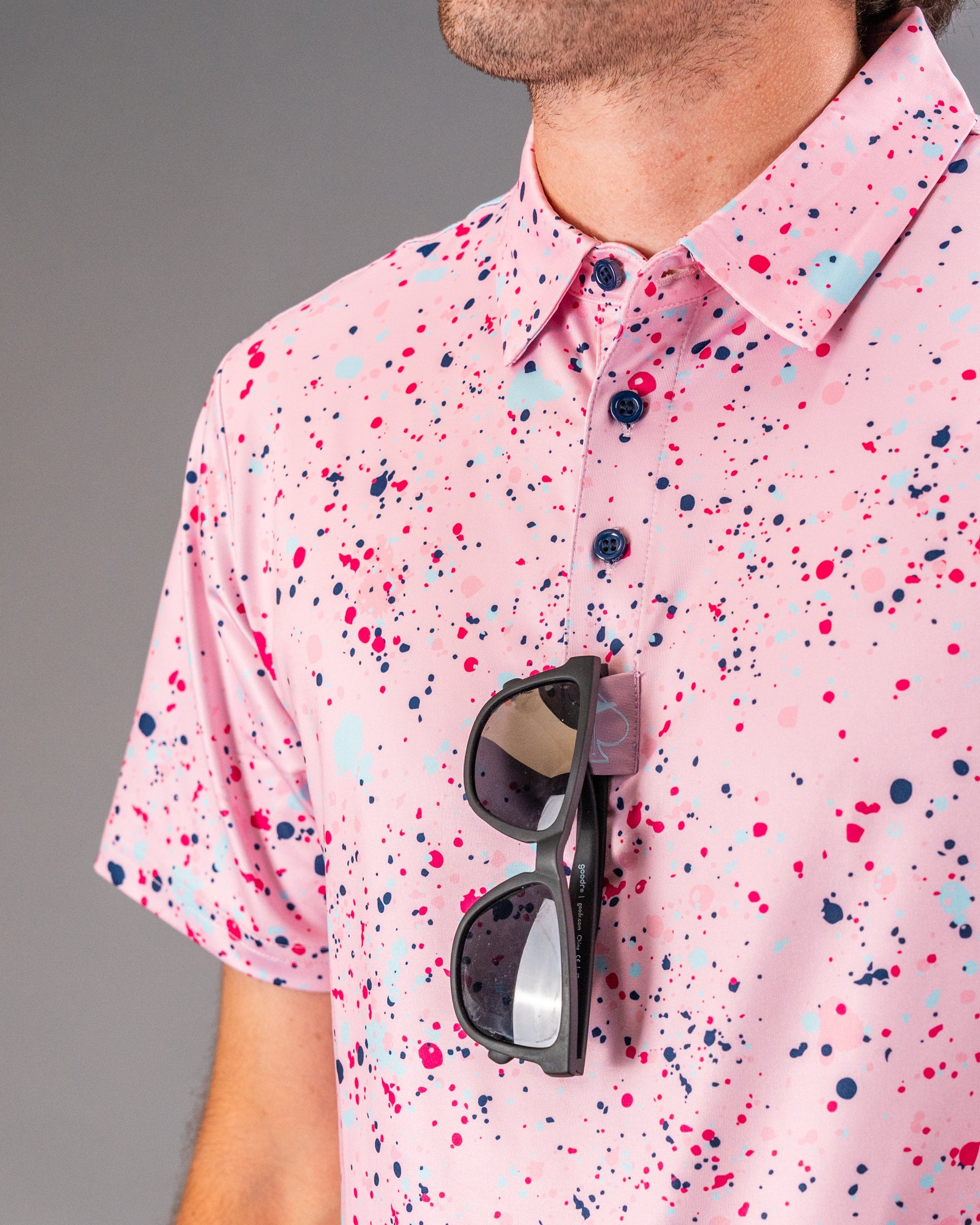 Men's pink splatter golf shirt featuring vibrant paint-like patterns, paired with stylish sunglasses for a bold look.