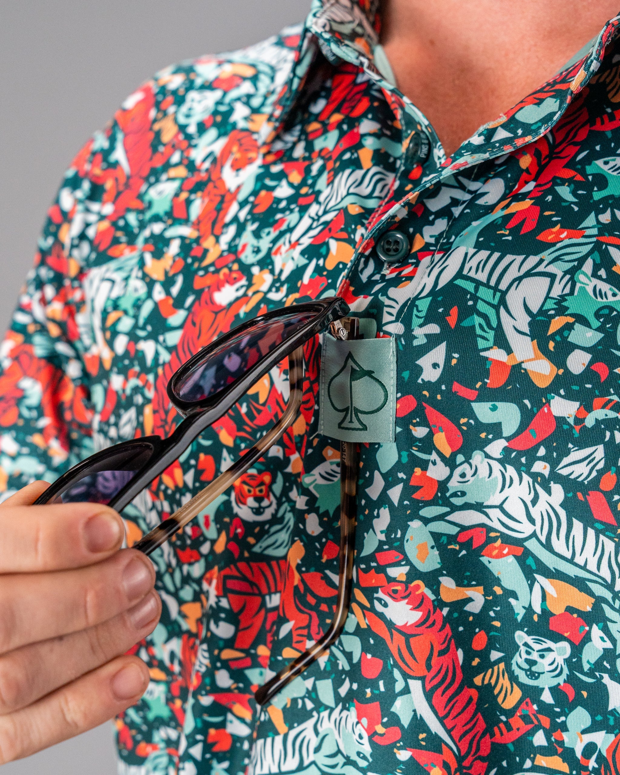 Bold Tiger Shatter Teal golf shirt featuring vibrant tiger and floral patterns, with sunglasses attached for a stylish look.