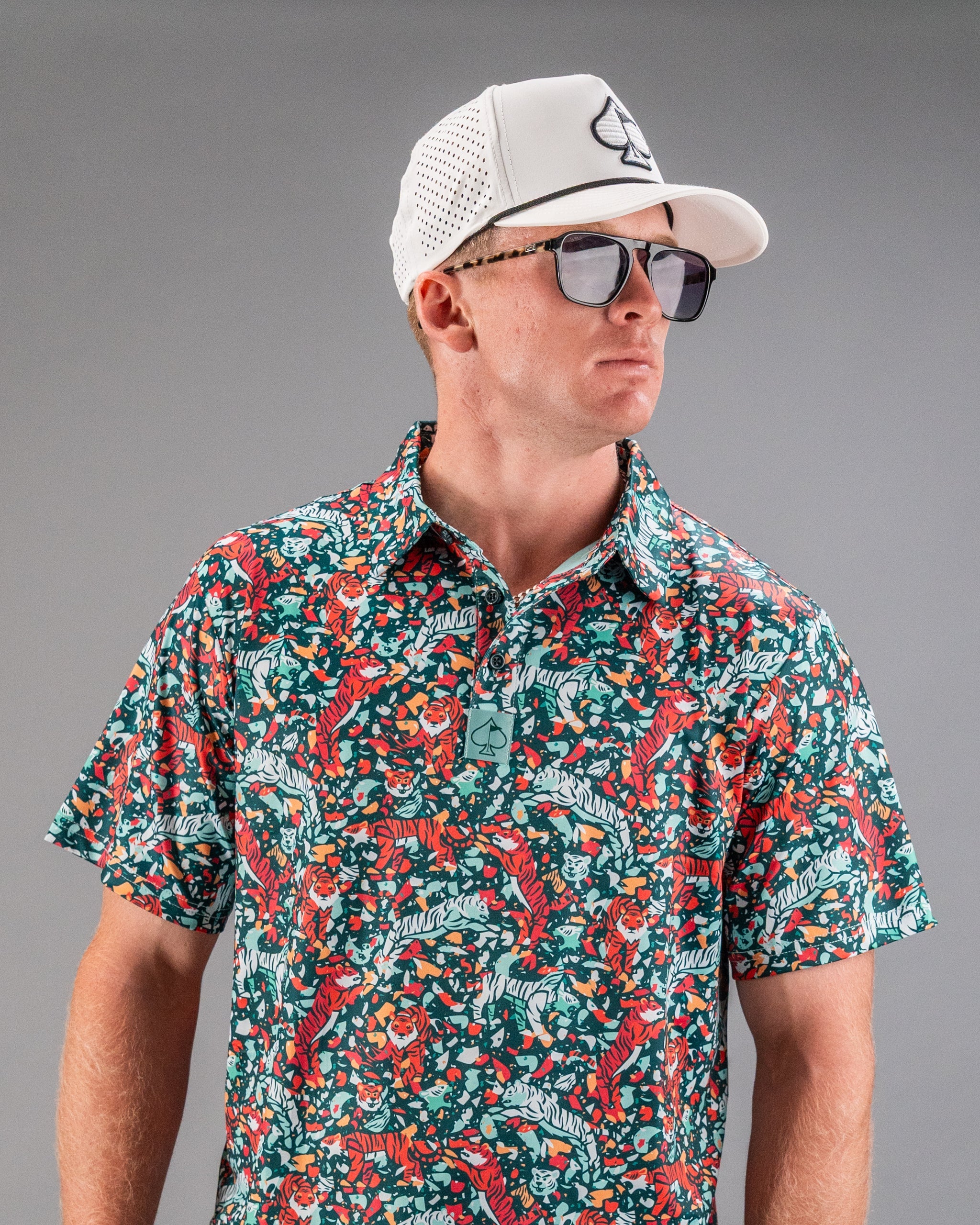 Bold teal golf shirt featuring a vibrant tiger and floral pattern, paired with a white cap and sunglasses. Perfect for stylish golfers.