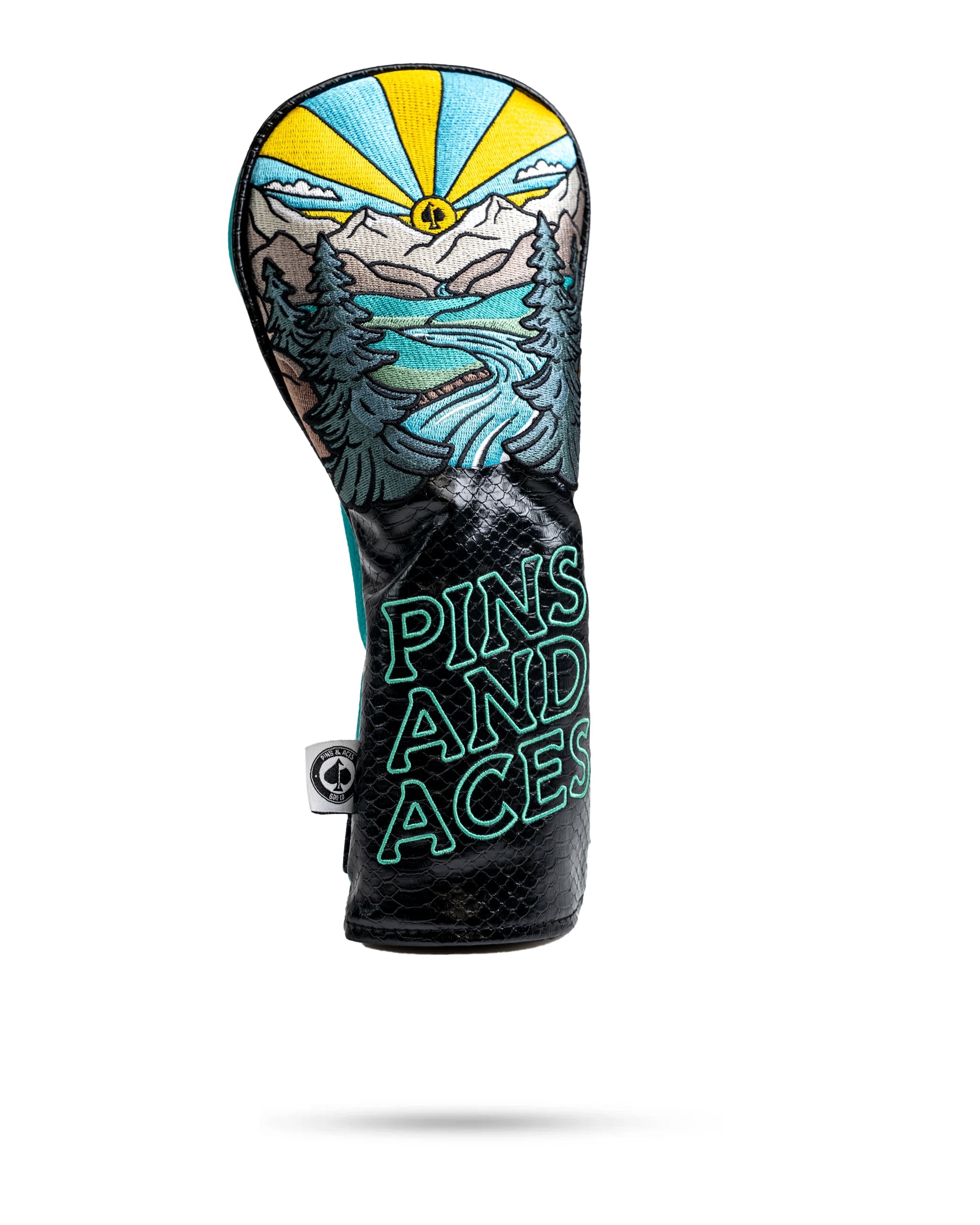 Colorful golf headcover with mountain, river, and sun design; black strap with "PINS AND ACES" in neon blue embroidery.