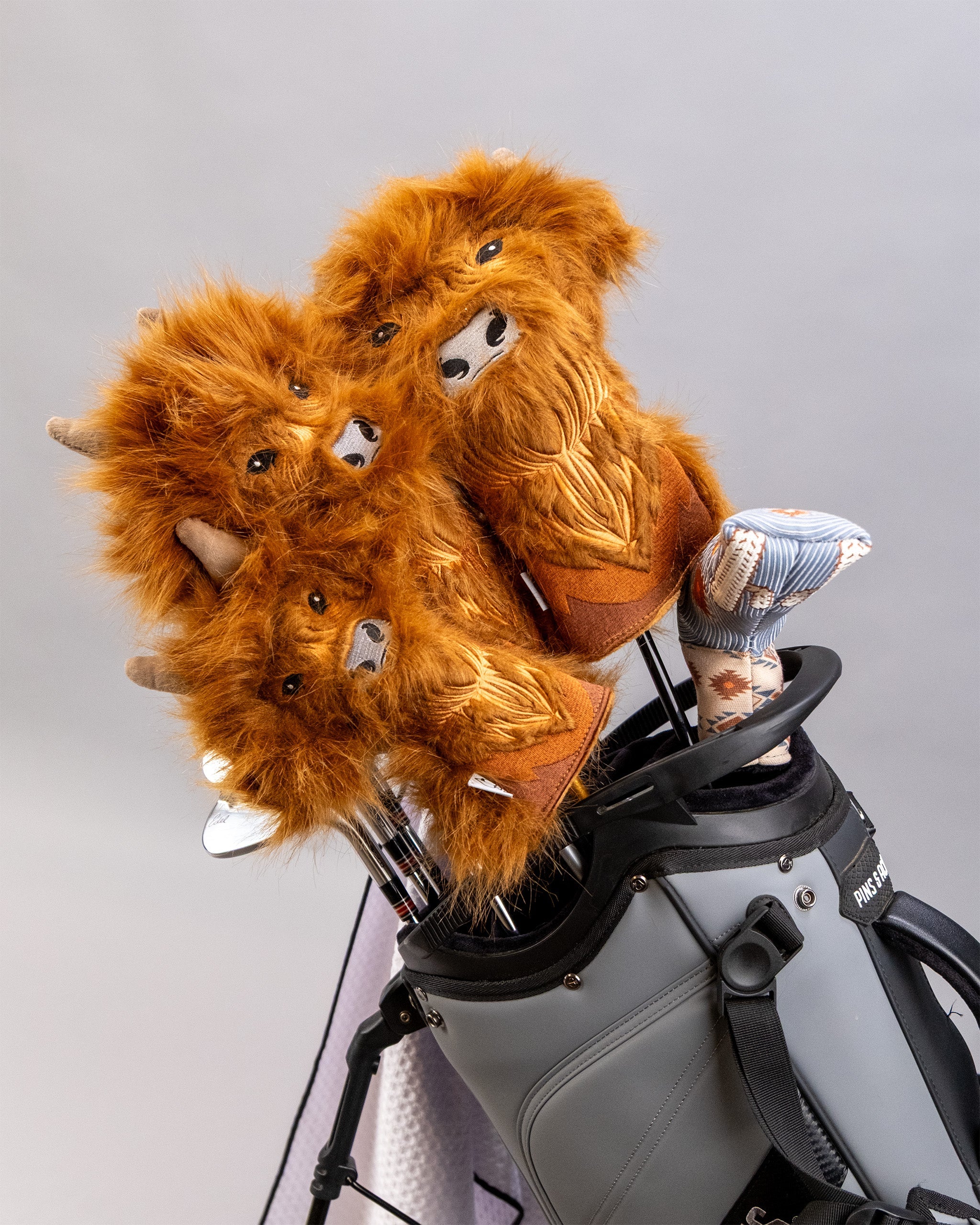 Highland Cow themed golf fairway cover with plush, furry texture and embroidered facial features, placed in a golf bag.