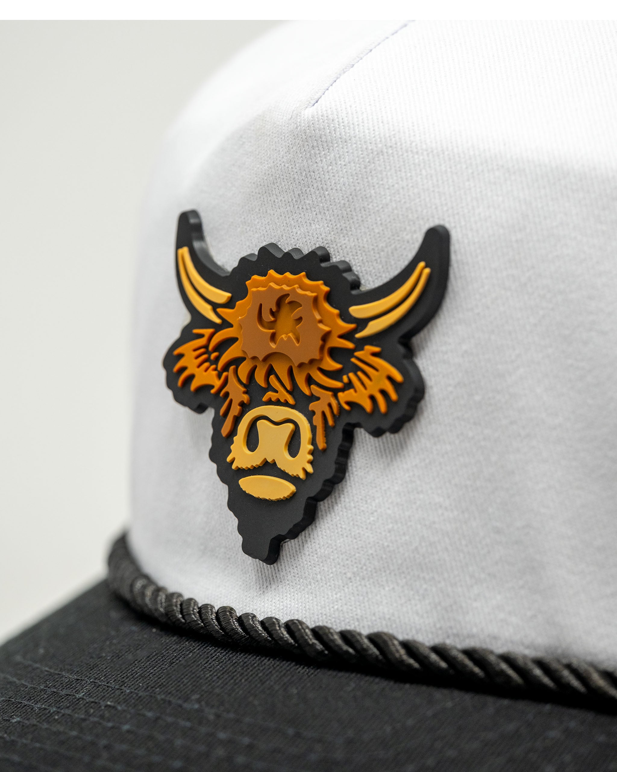 Heritage Rope Hat featuring a Highland Cow design in orange and black, mounted on a white fabric background.