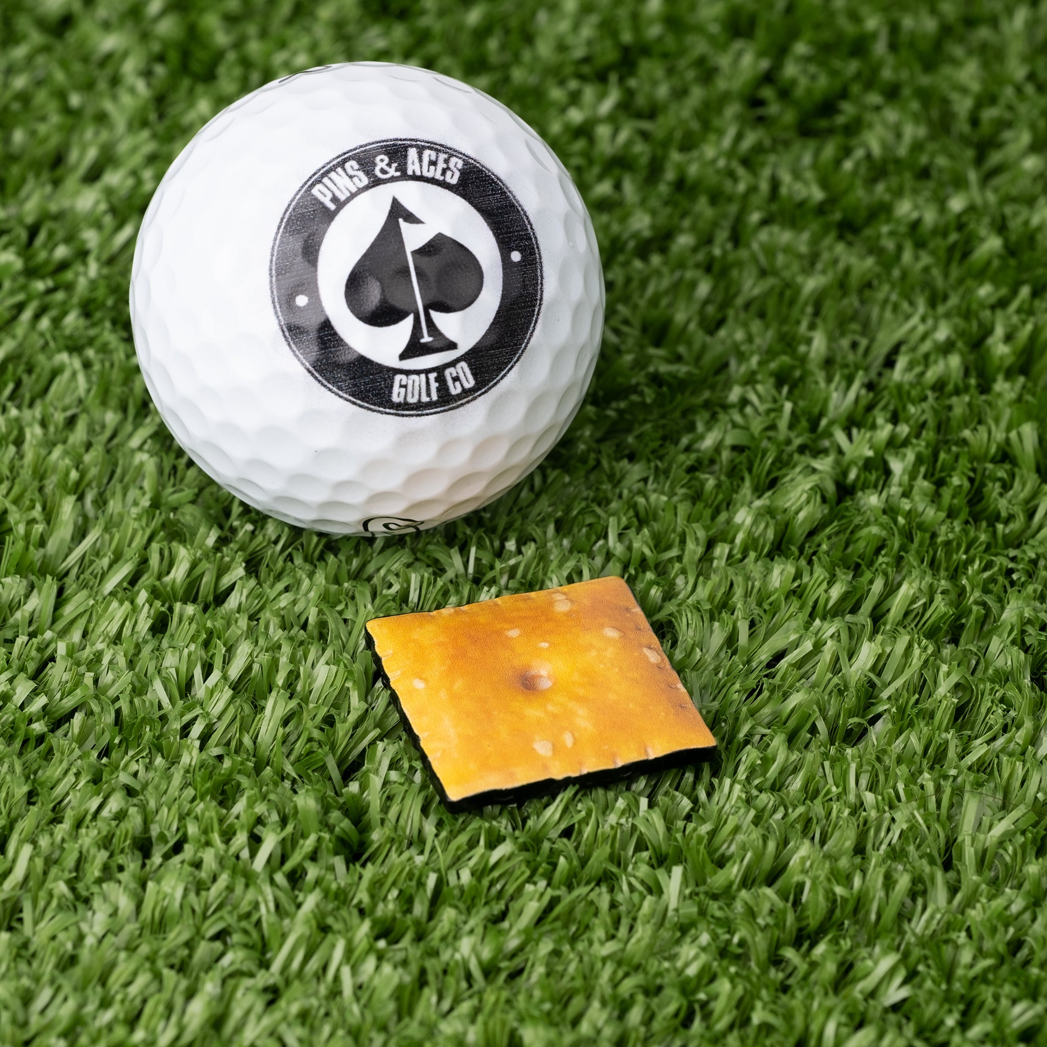 Cheese Cracker Ball Marker featuring a realistic cheese design, positioned next to a golf ball on a grassy surface.