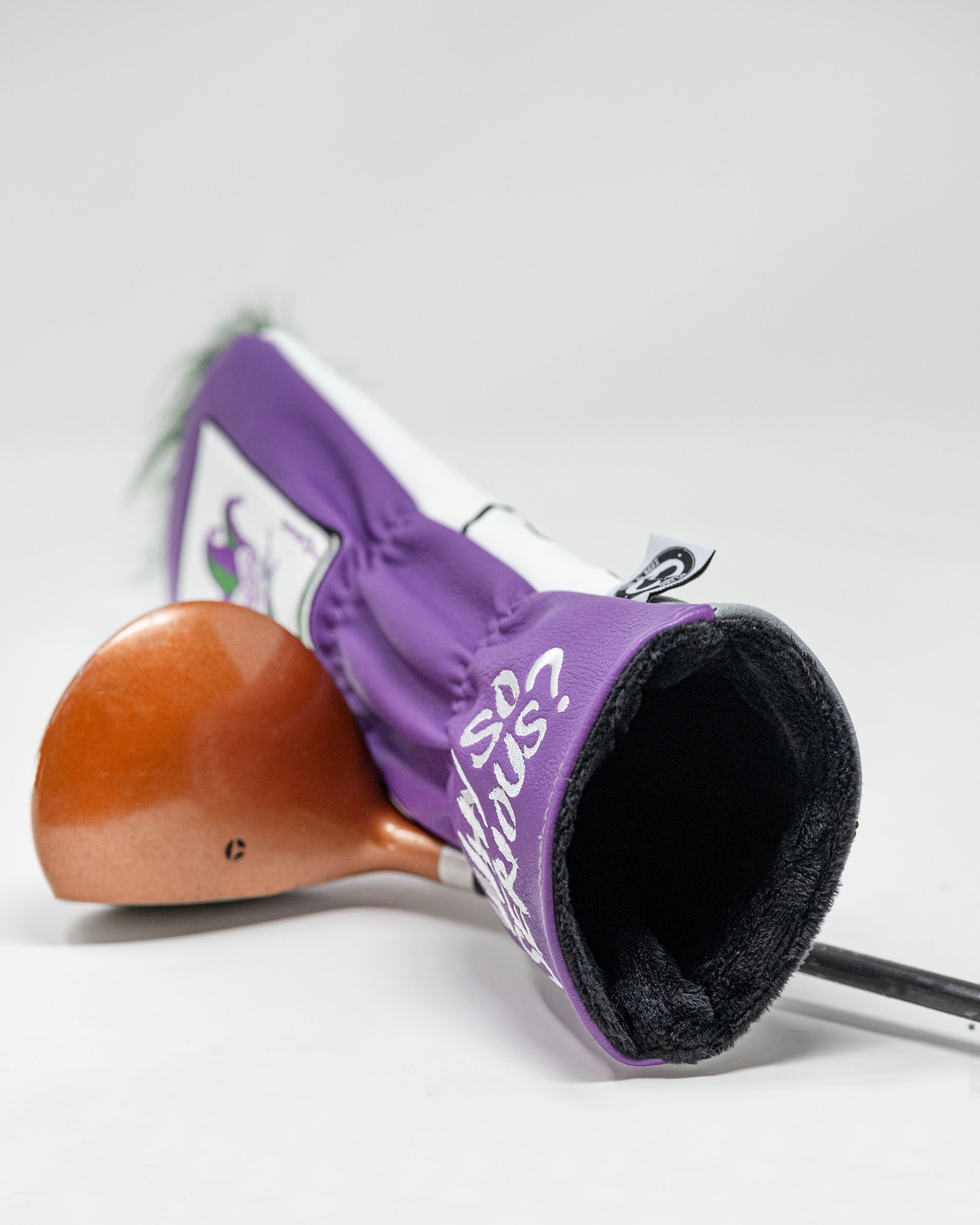 Purple golf club headcover with a playful dragon logo, partially covering a copper-colored golf club, on a white background.