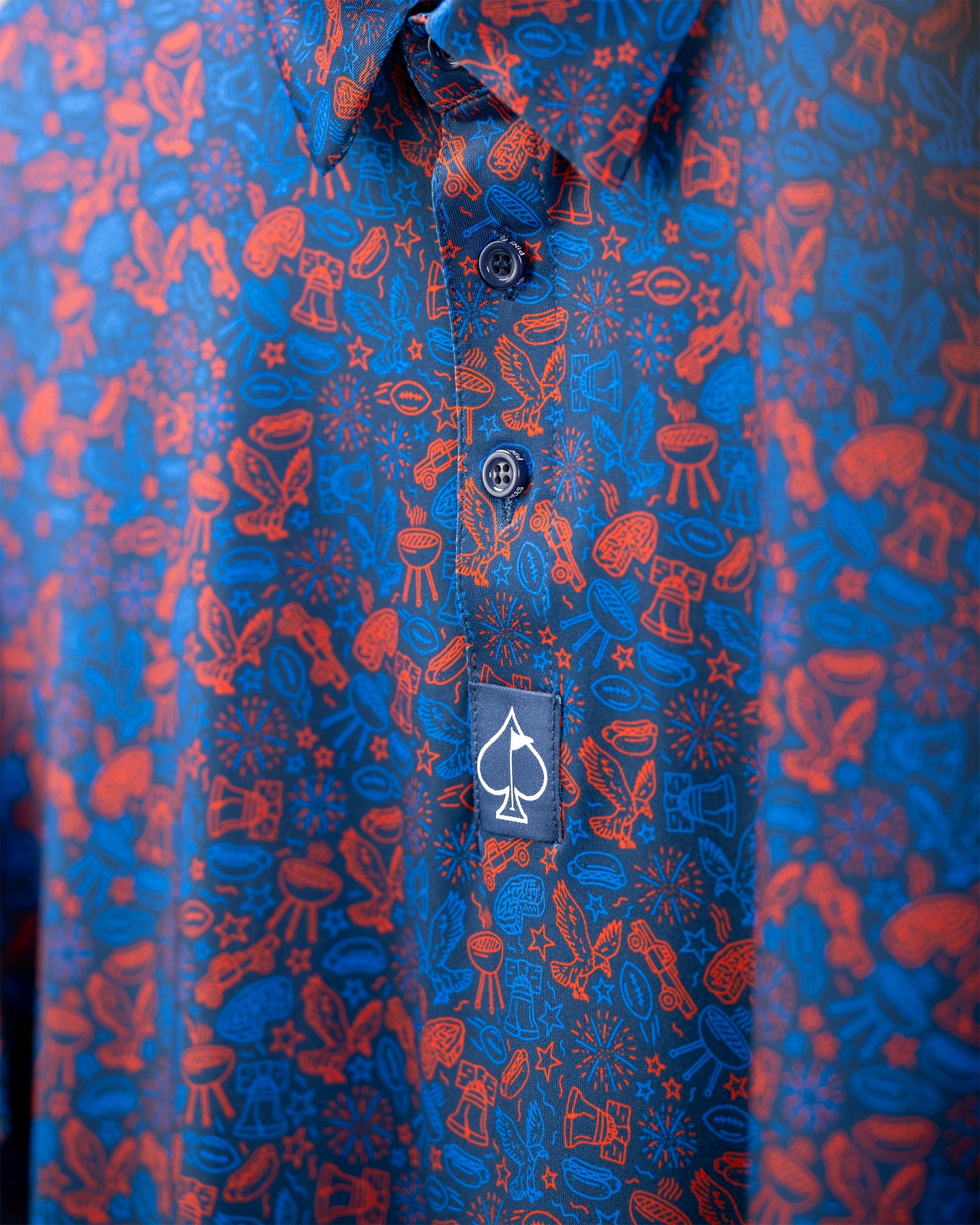 Navy golf shirt featuring a vibrant red doodle pattern with playful icons, including grills and stars, and a logo tag.