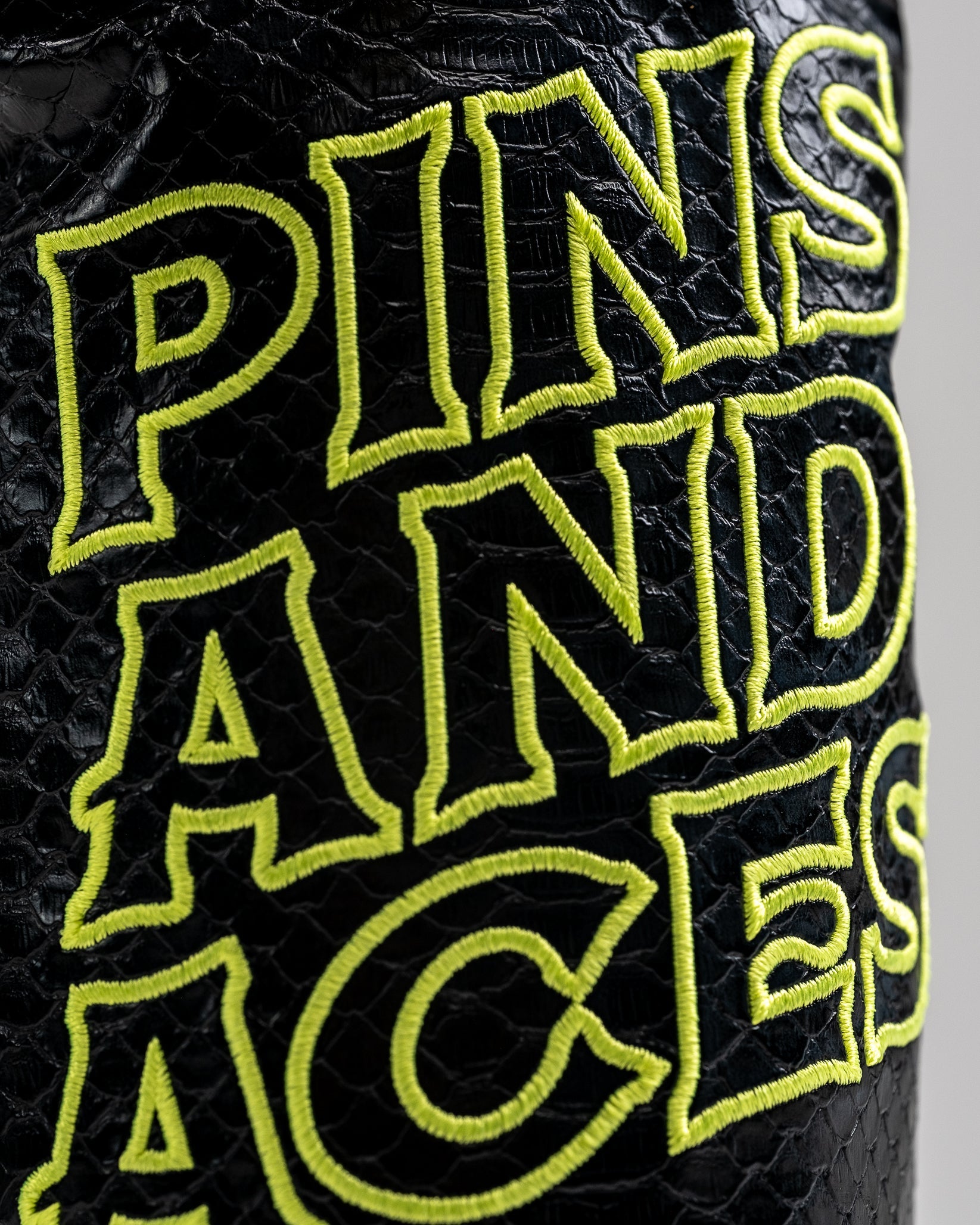 Close-up of bold, neon yellow embroidered "PLANTS AND" text on textured black faux leather golf accessory.