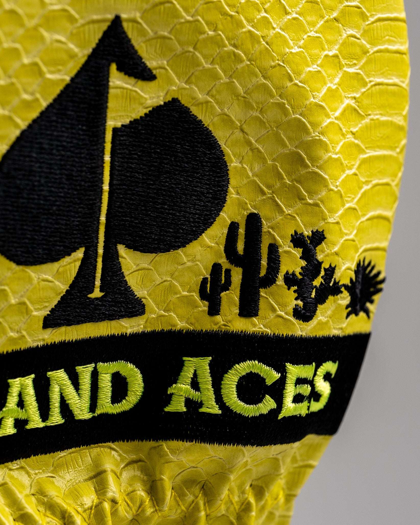 Close-up of a yellow textured golf accessory with black embroidered spade, cacti, and "LAND ACES" text for bold golf style.