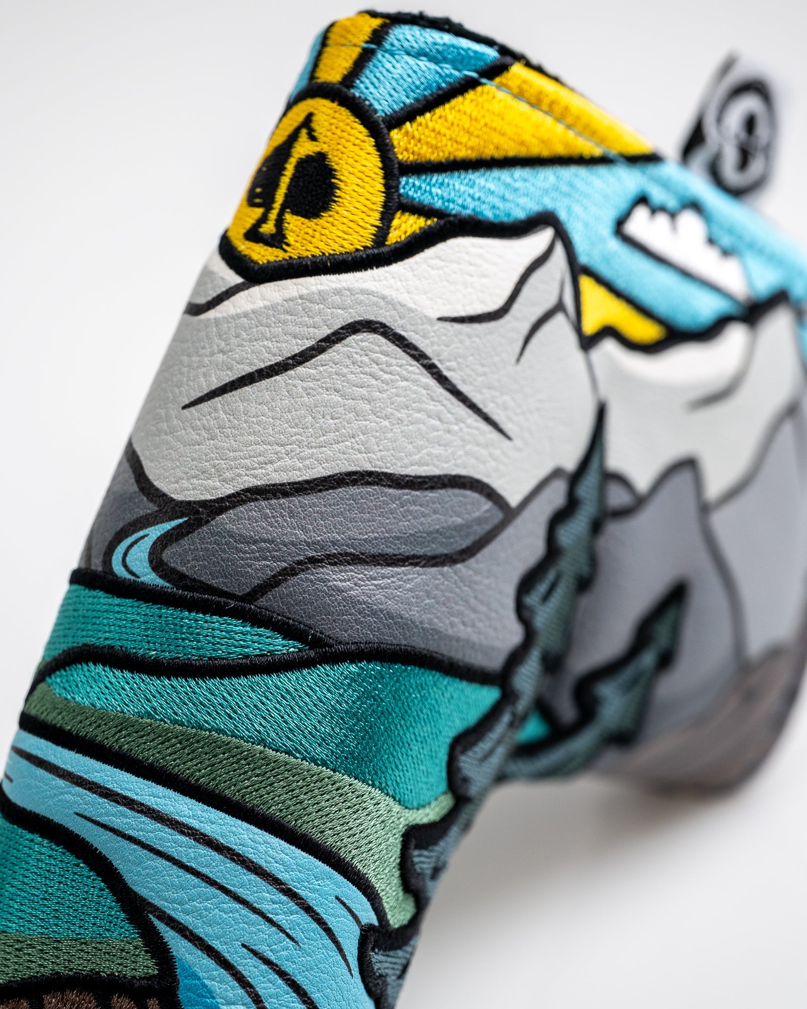 Close-up of a bold, colorful golf headcover featuring mountain, wave, and sun designs in blue, yellow, gray, and black emb...