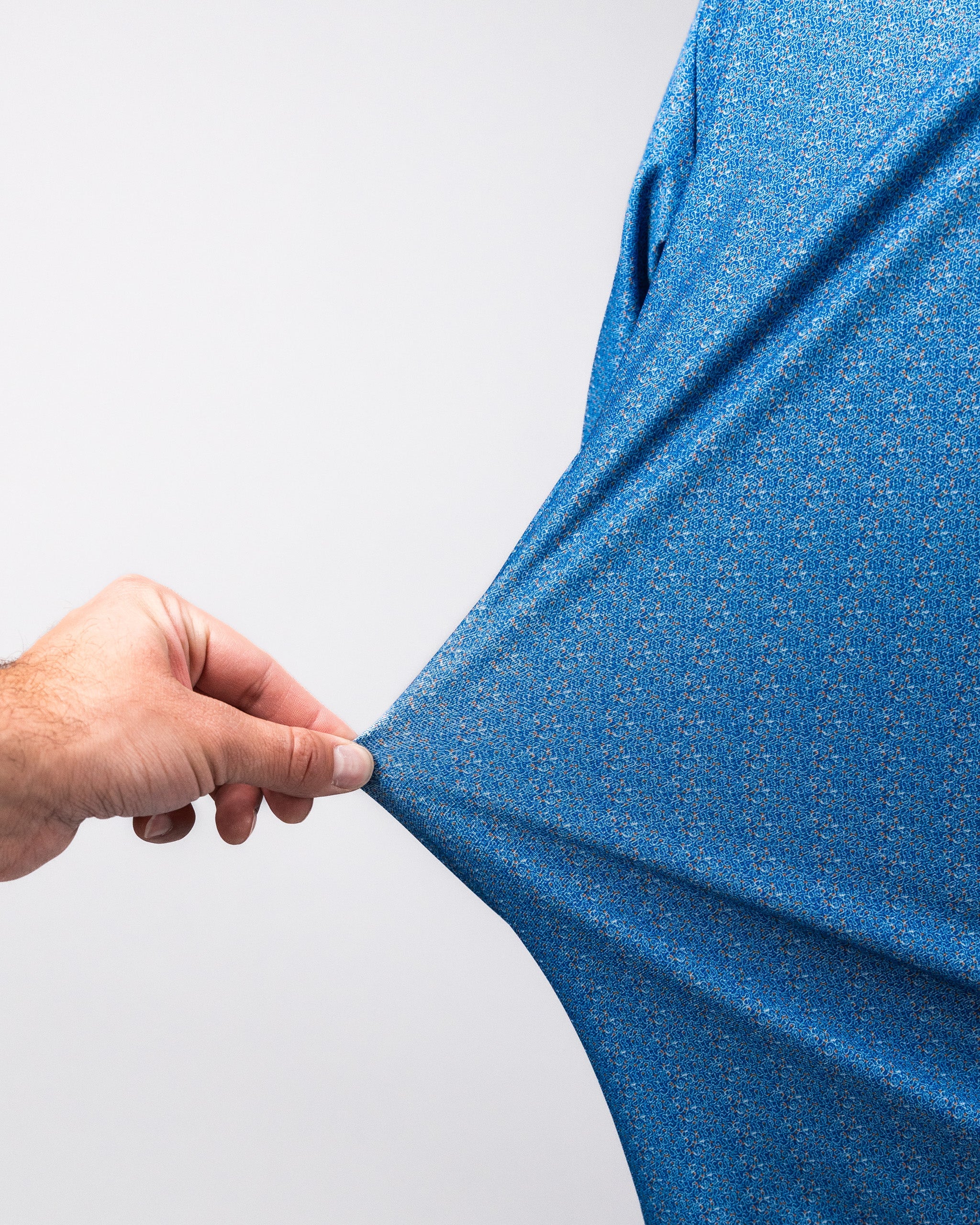 Close-up of a hand stretching a blue Player Preferred™ Polo - Cosmic Swirl fabric, showcasing its vibrant, textured pattern.