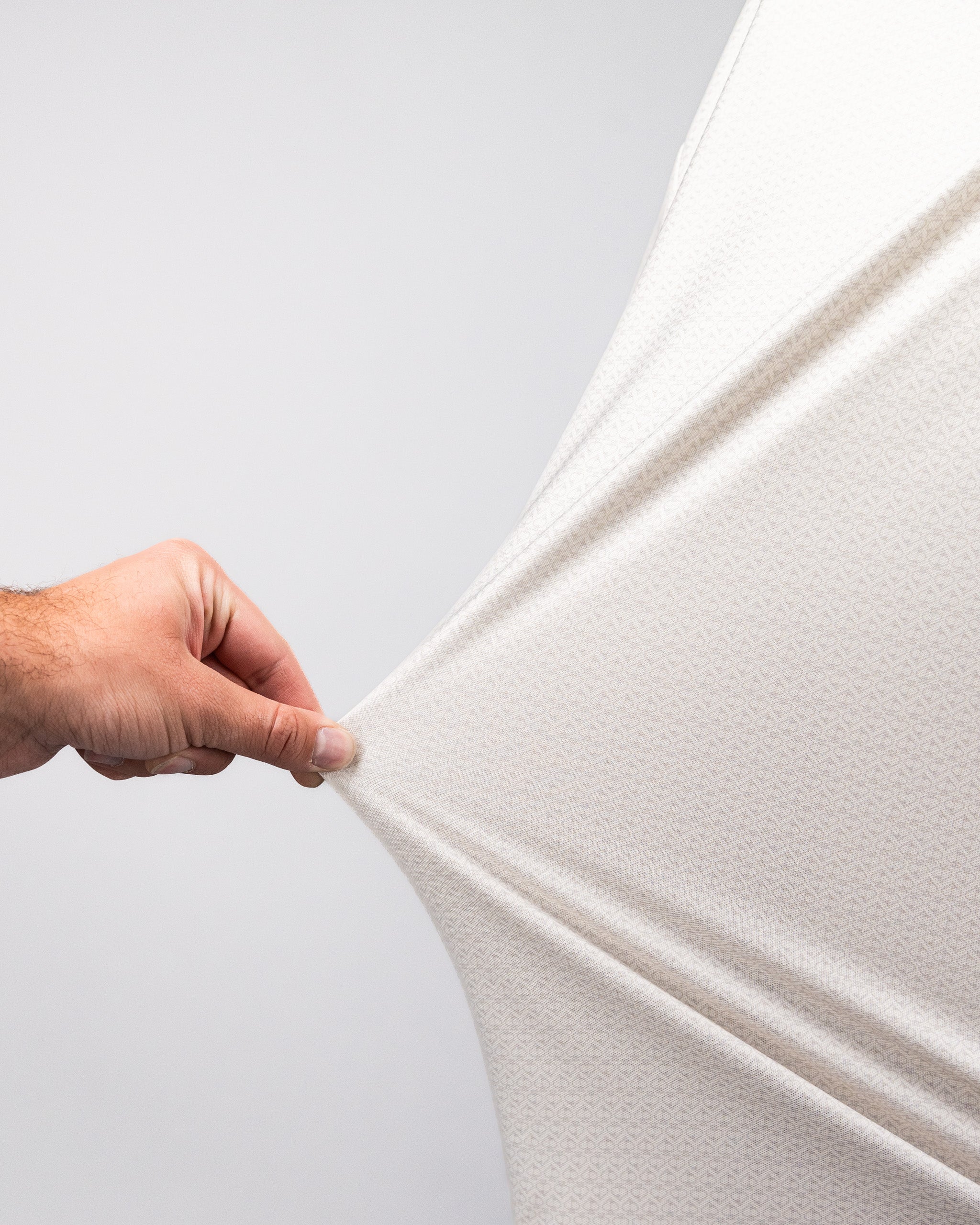 Close-up of a hand stretching a white Player Preferred™ Polo - Vapor Spade fabric, showing its stretchability and texture.