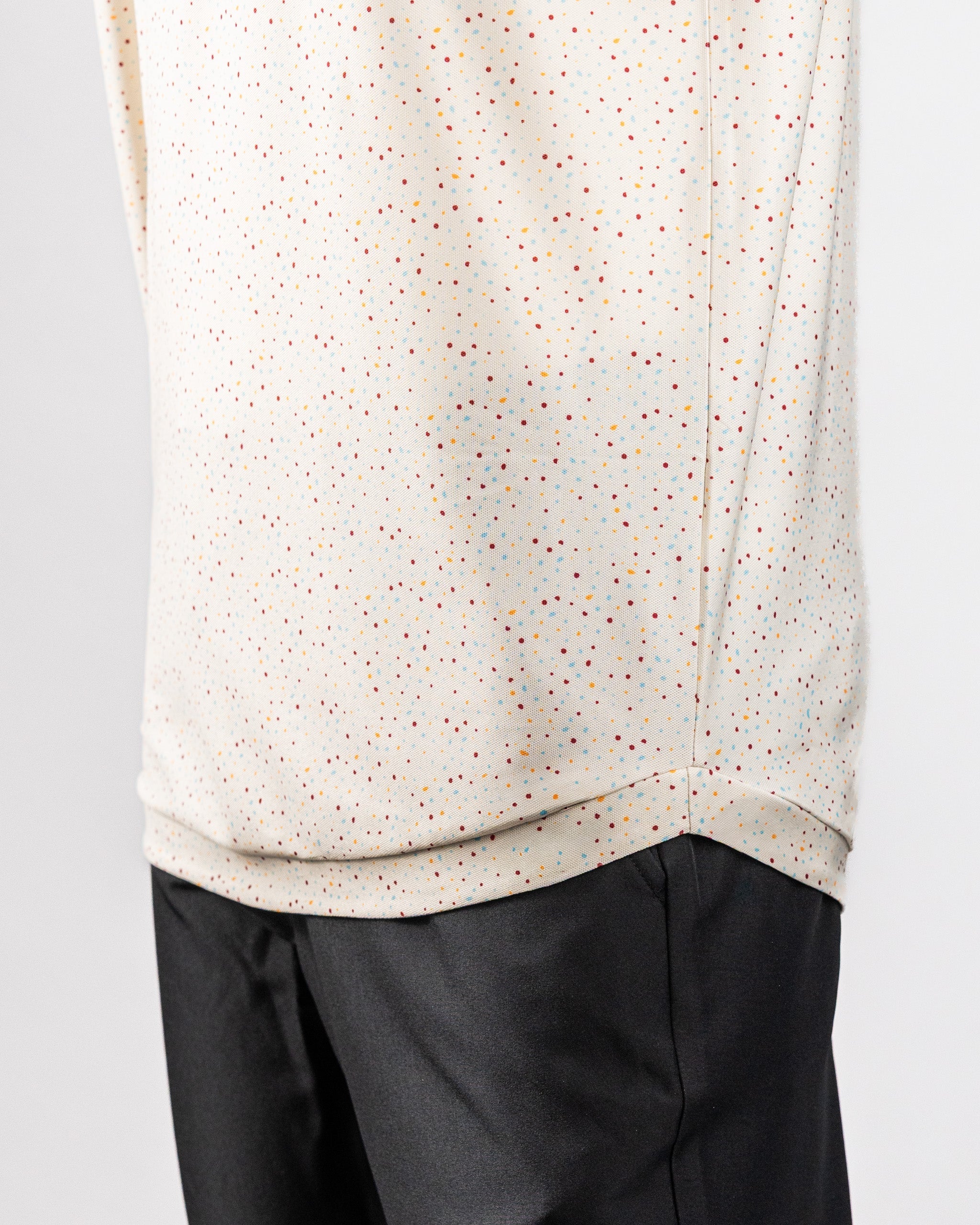 Close-up of a Player Preferred™ Polo in Terrazzo pattern, featuring a white fabric with multicolored speckles, paired with black pants.