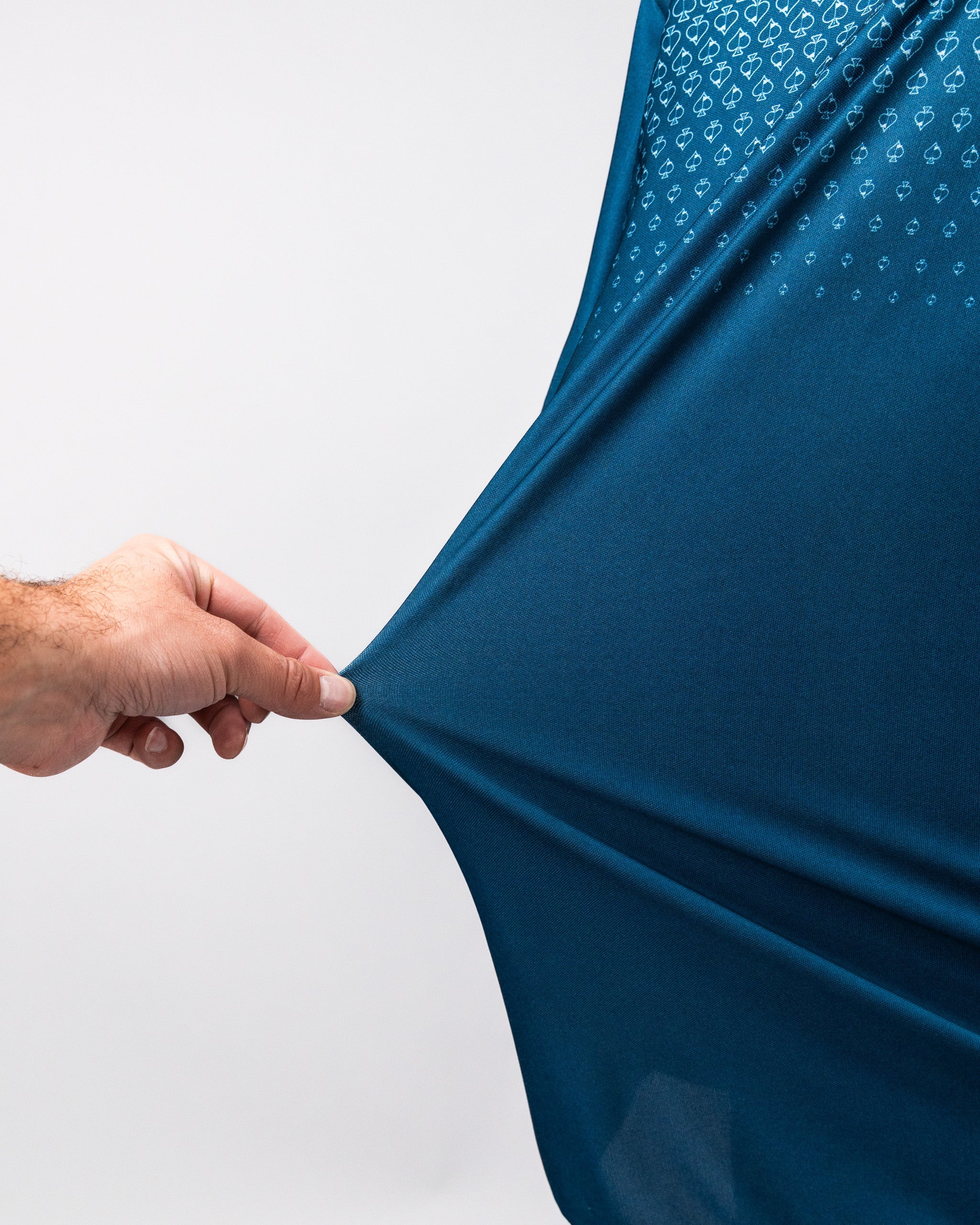 Close-up of a hand stretching a navy Player Preferred™ Polo shirt with Spade Fade pattern, showing the fabric's stretch and texture.