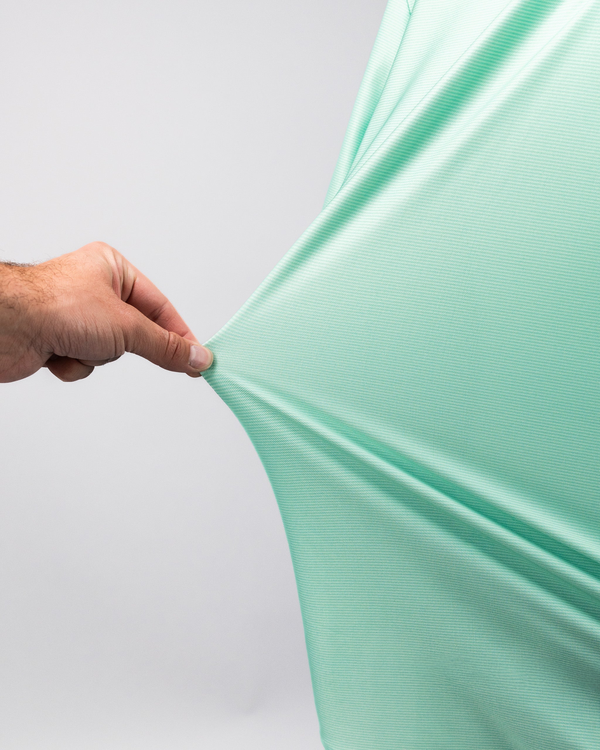 Close-up of a hand stretching a mint green Player Preferred™ Polo with spearmint stripes fabric, showing its smooth, stretchy material.