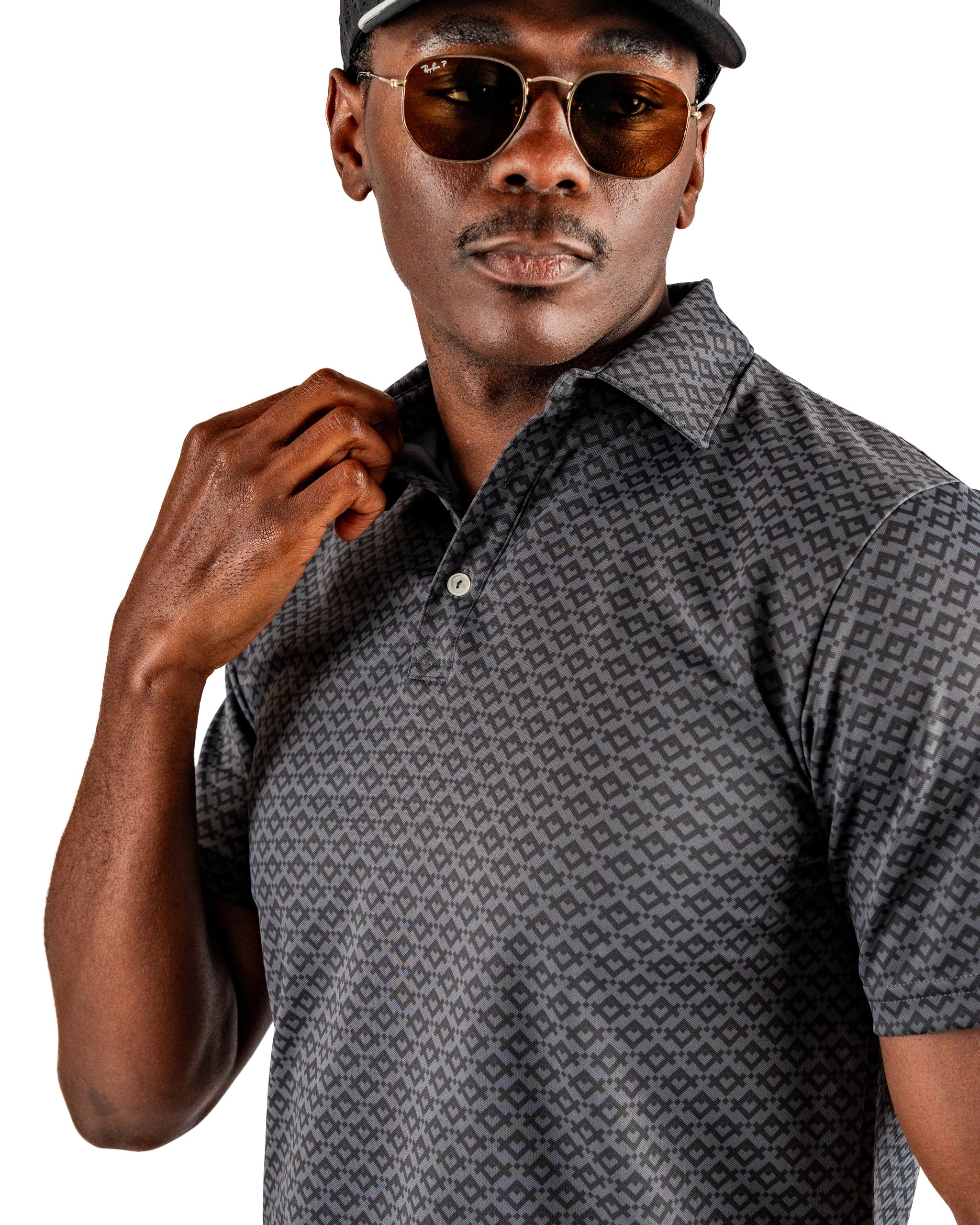 Stylish man wearing a slate mosaic patterned polo shirt and sunglasses, showcasing bold golf apparel for standout performance.