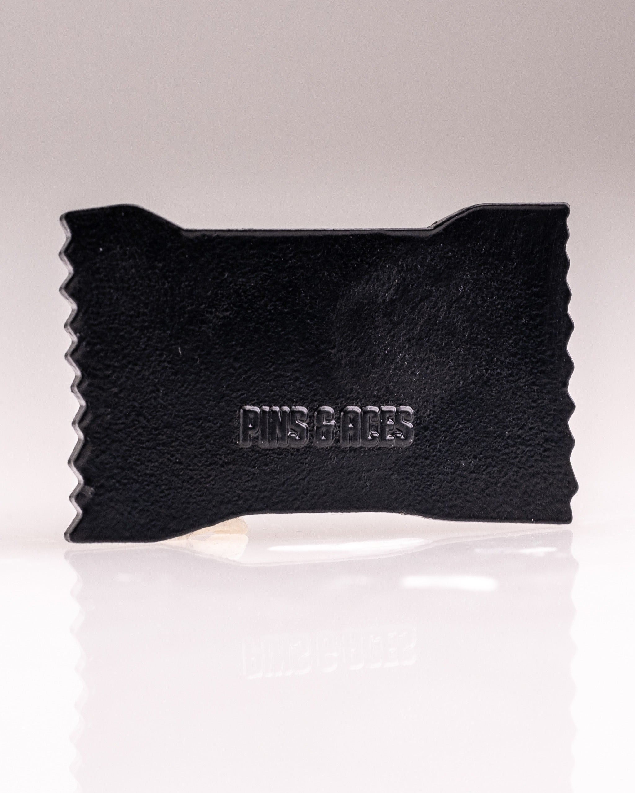 Black Baby Ruth® ball marker featuring a textured design with "Pins & Aces" embossed for a stylish touch on the golf course.