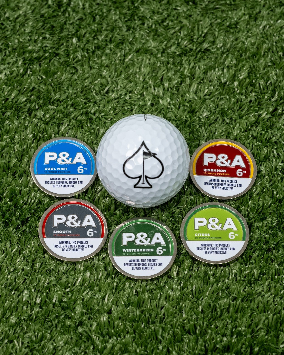 Cool Mint ball marker from Pins and Aces surrounded by four other colorful markers on a golf course green.