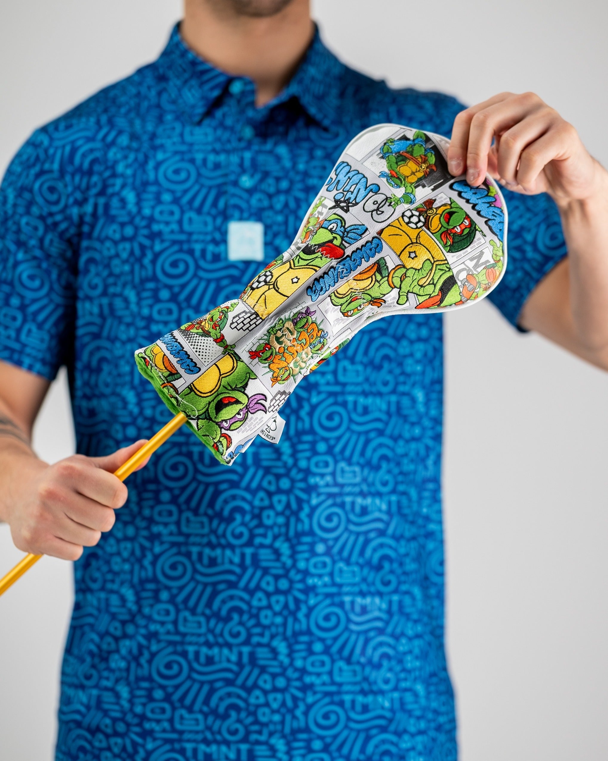 Colorful TMNT-themed headcover featuring doodle-style artwork, held by a person in a blue patterned polo shirt.