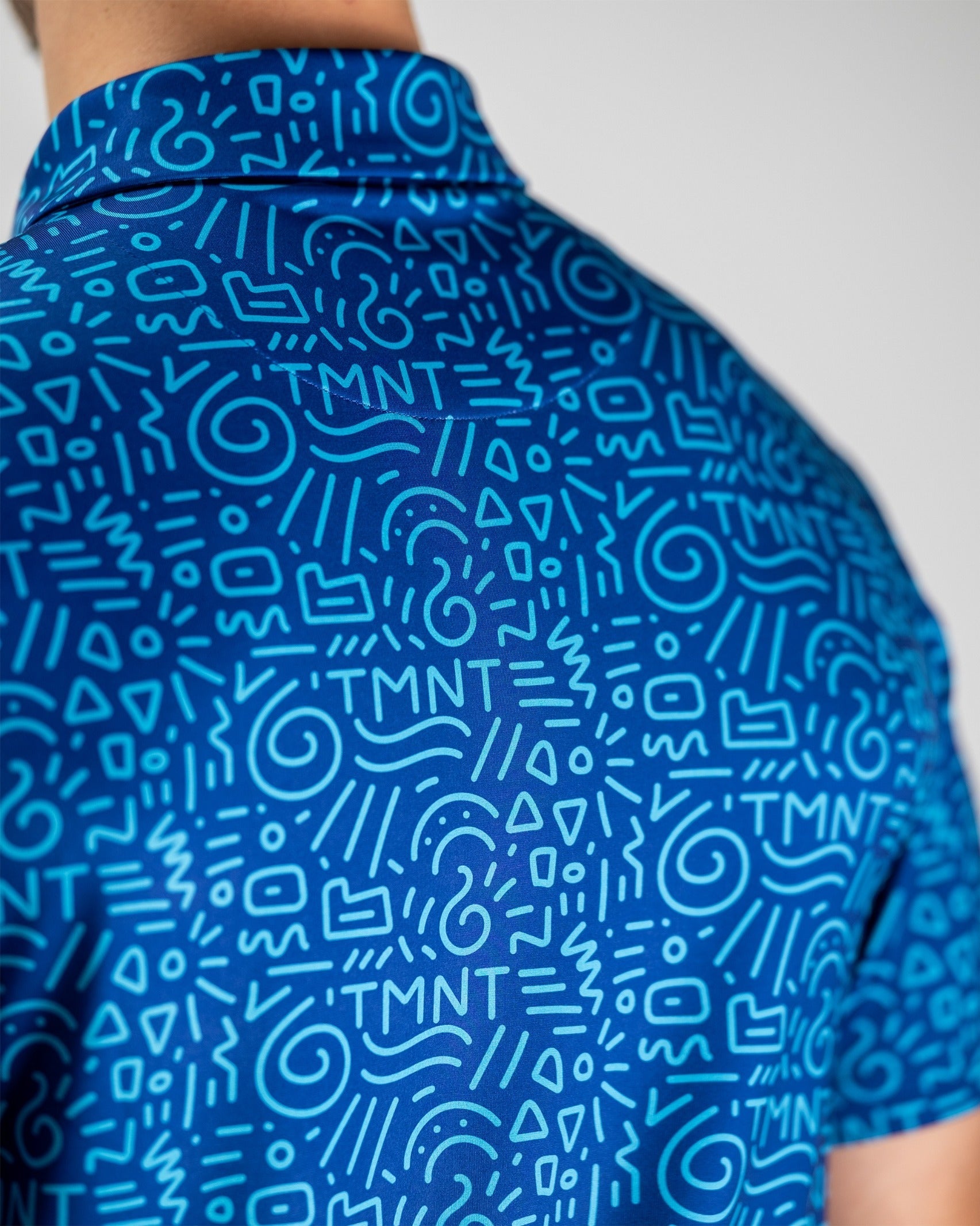 Bold blue golf shirt featuring a playful doodle pattern with TMNT graphics, perfect for fans wanting to stand out on the course.