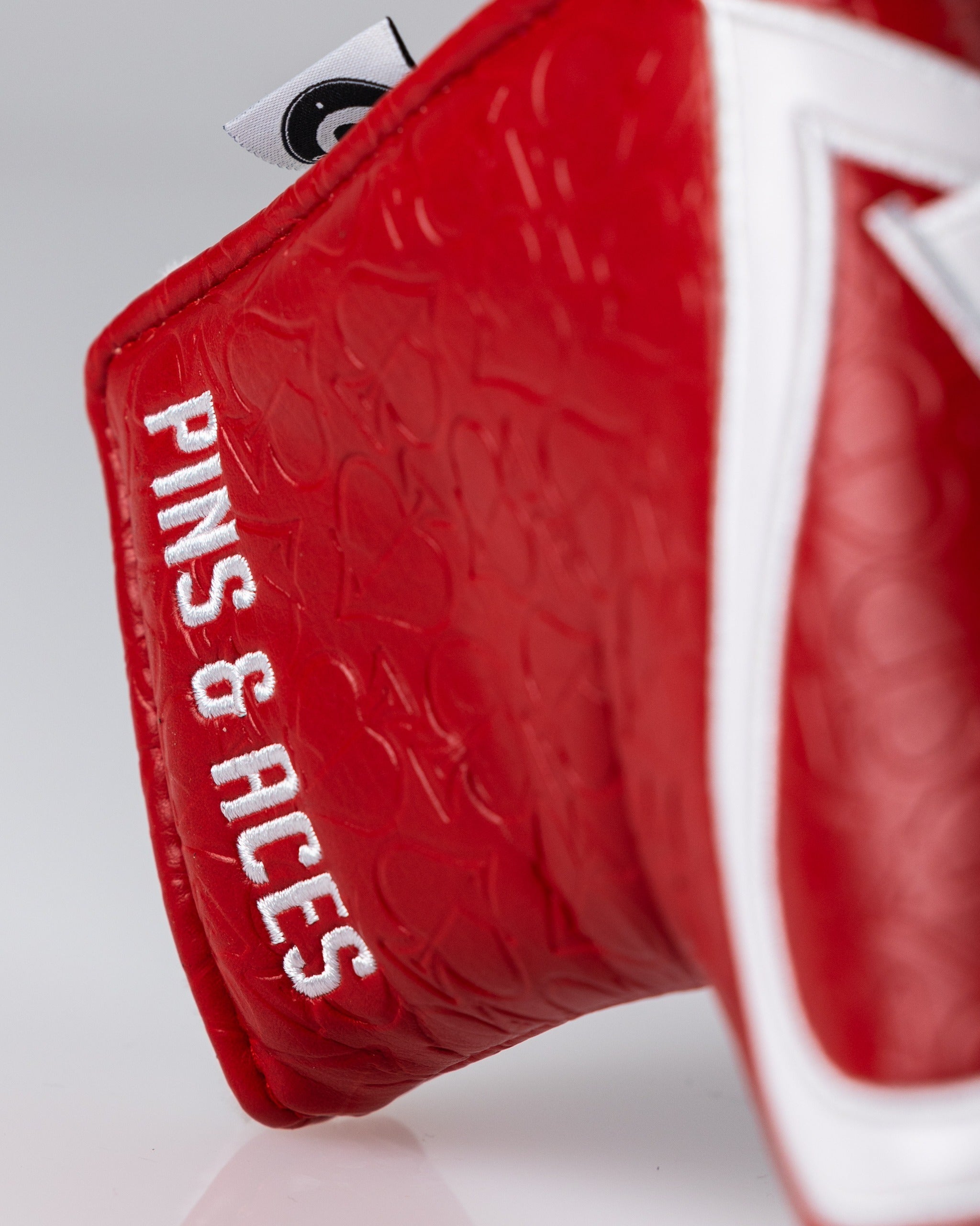 Red golf headcover with textured pattern, white zipper, and "PINS & TACKS" embroidered in white. Perfect for bold golf style.