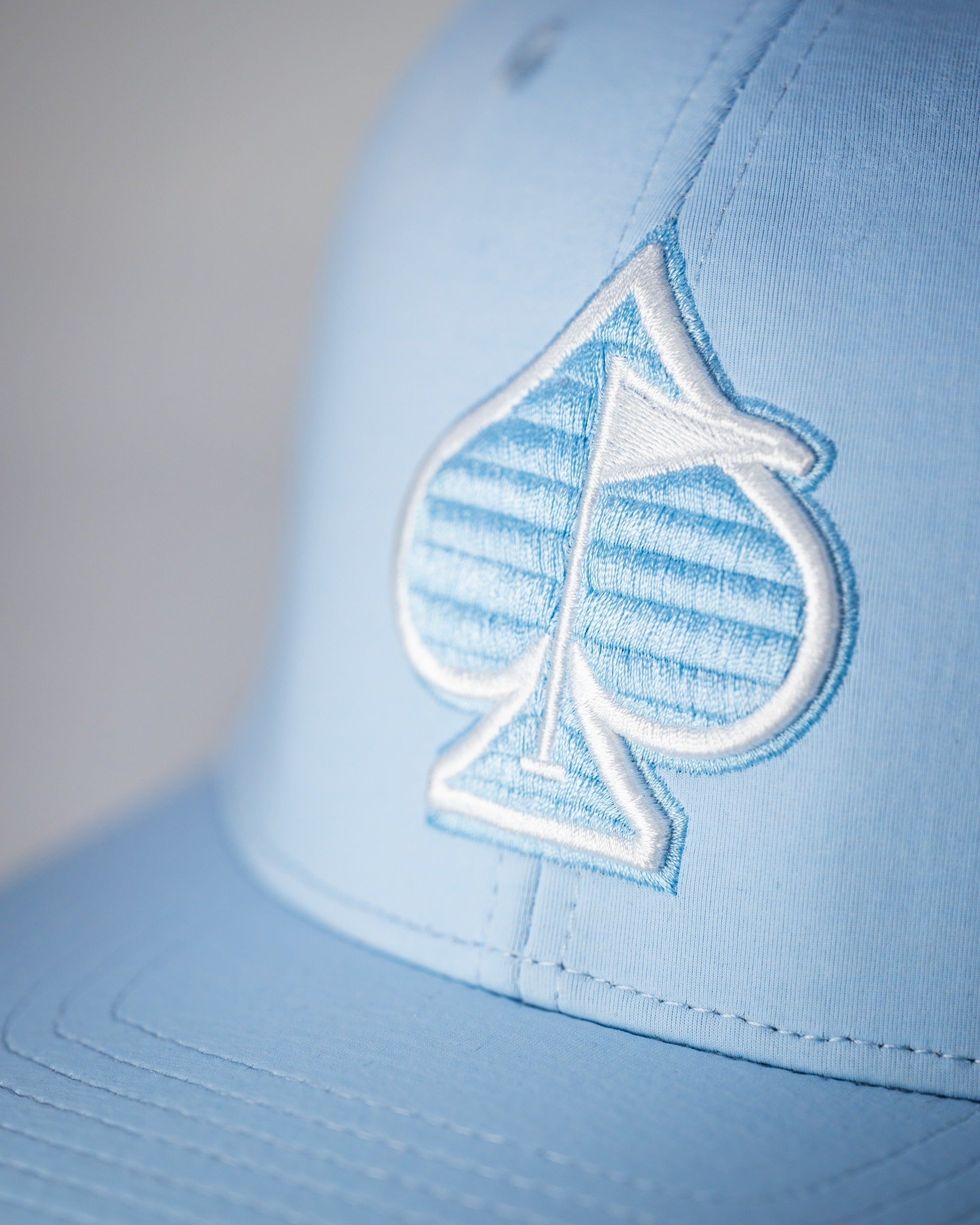 Carolina blue performance hat featuring a textured spade logo, perfect for stylish golfers on the course.