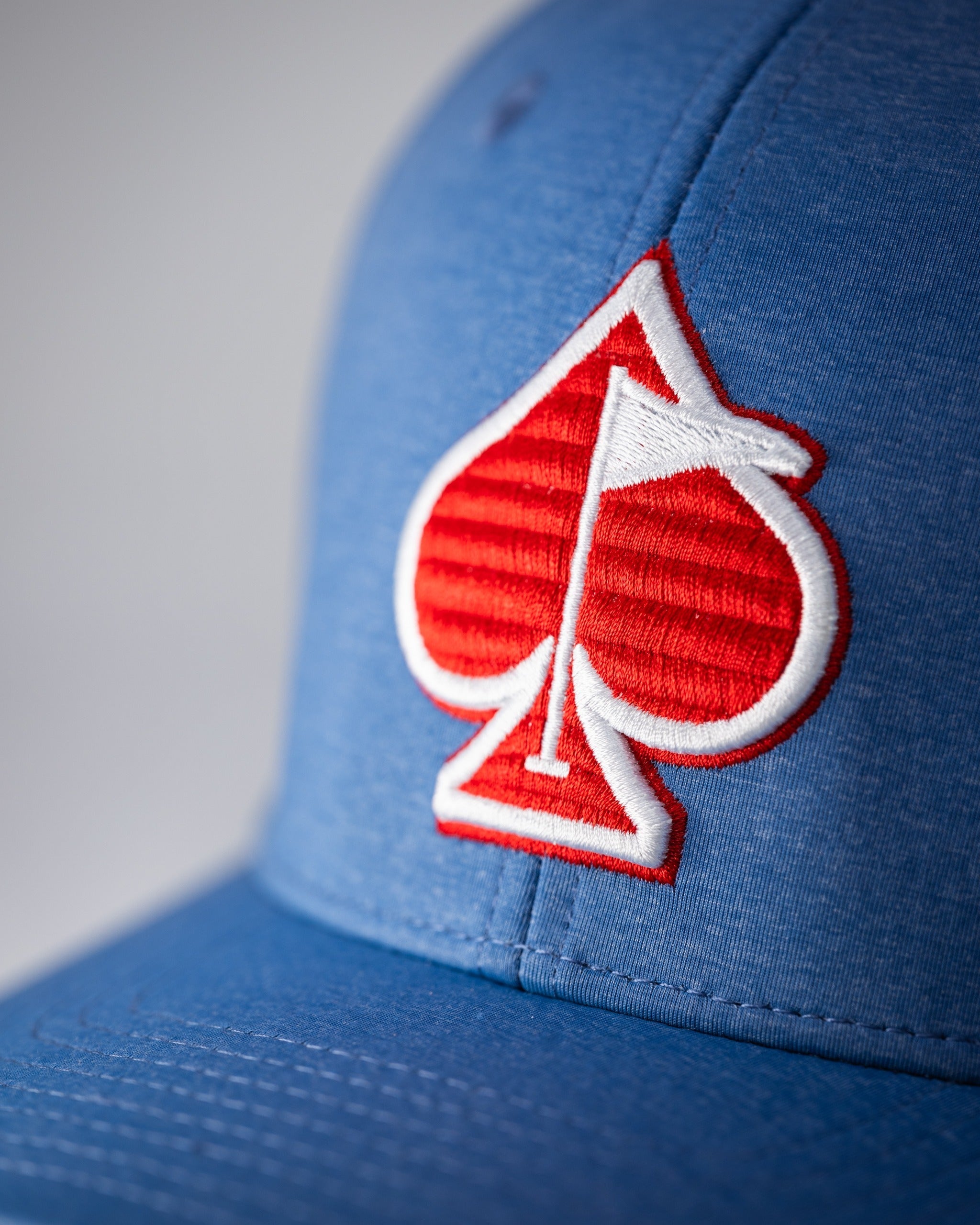 Blue Performance Spade Hat featuring a bold red spade logo, designed for stylish golfers seeking standout apparel.