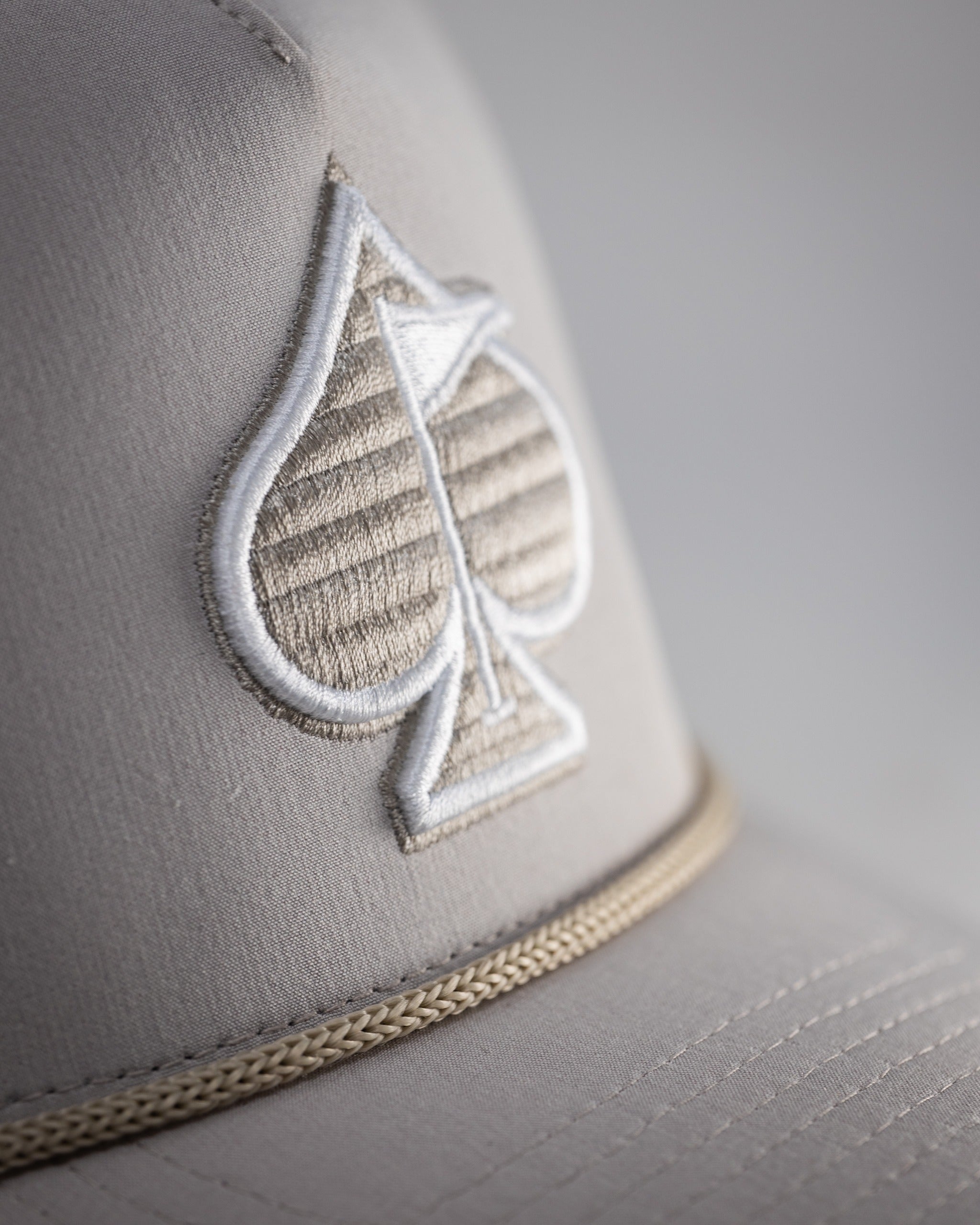 Perforated rope hat in bone color featuring a stylish embroidered spade logo and a classic rope detail.