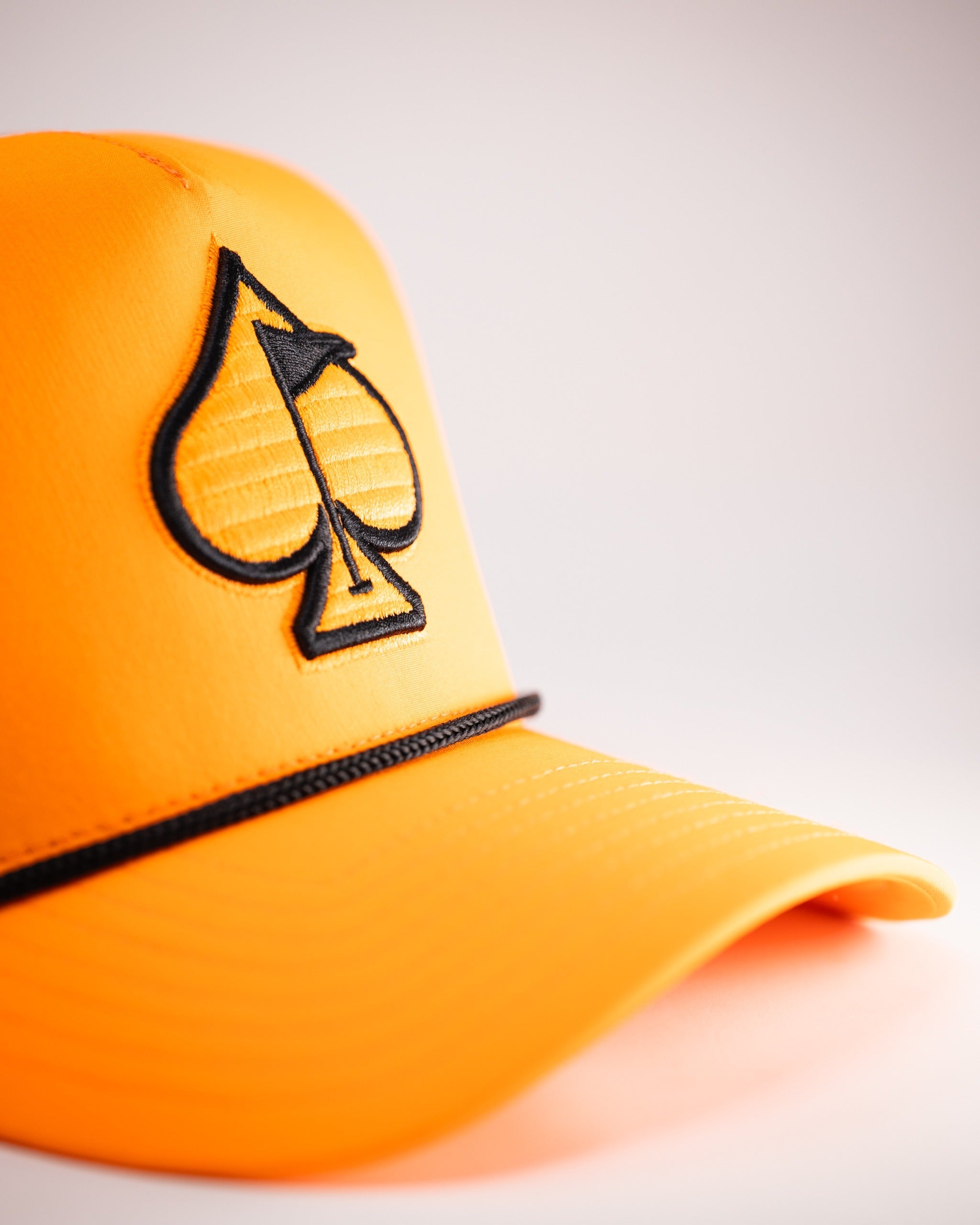 Highlighter orange perforated rope hat featuring a black spade logo and stylish design for bold golf enthusiasts.