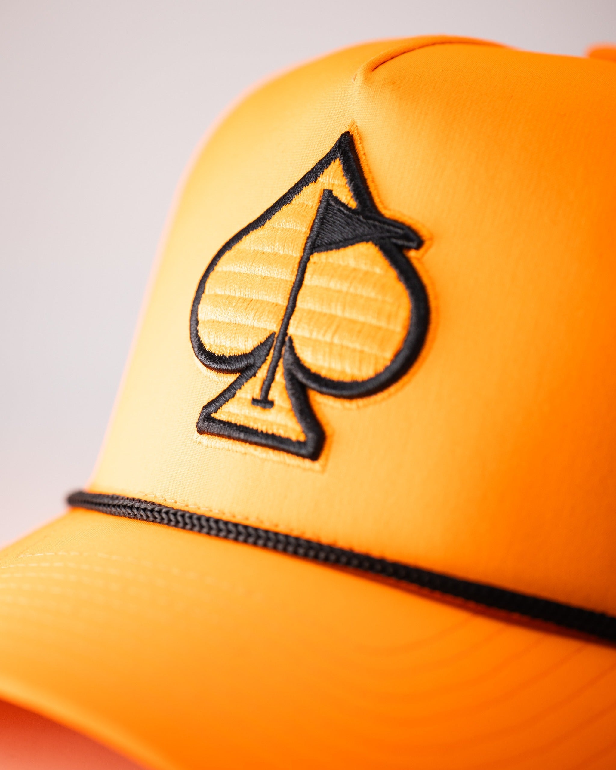 Highlighter orange perforated rope hat featuring a black spade logo and a stylish black band. Perfect for bold golfers.