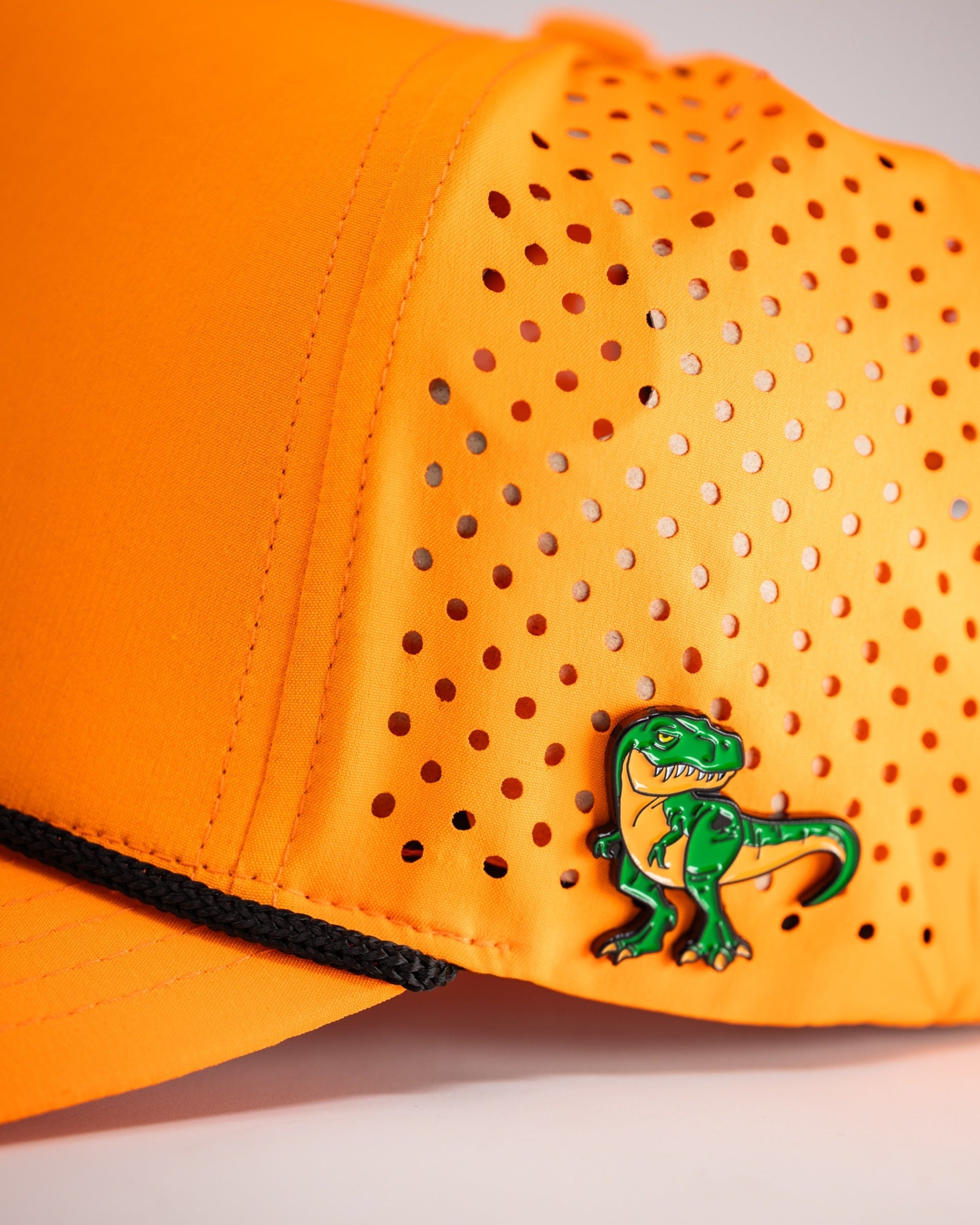 Highlighter orange perforated rope hat featuring a playful dinosaur pin, perfect for bold golfers seeking style.