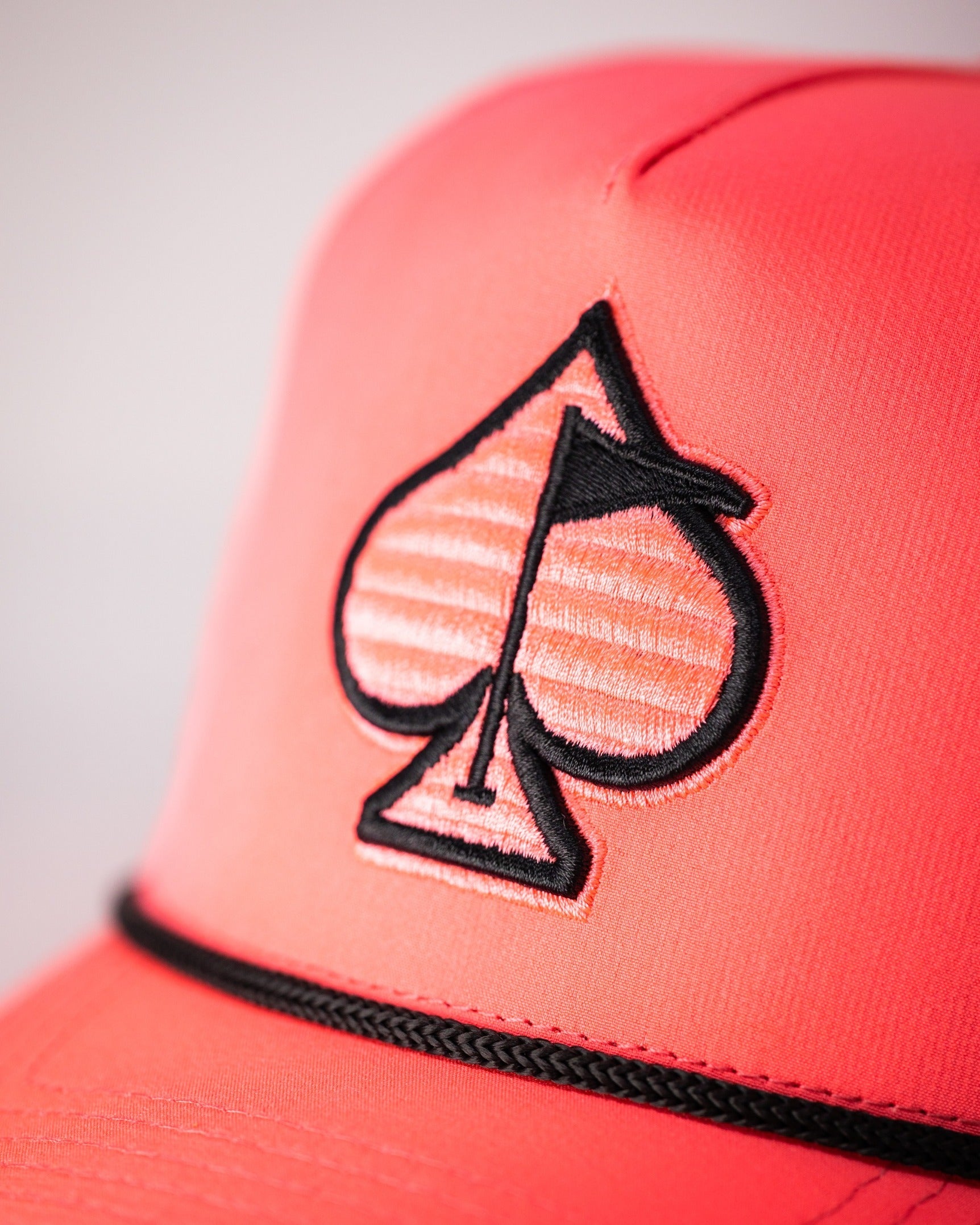 Highlighter pink perforated rope hat featuring a black spade logo, perfect for stylish golfers seeking standout accessories.