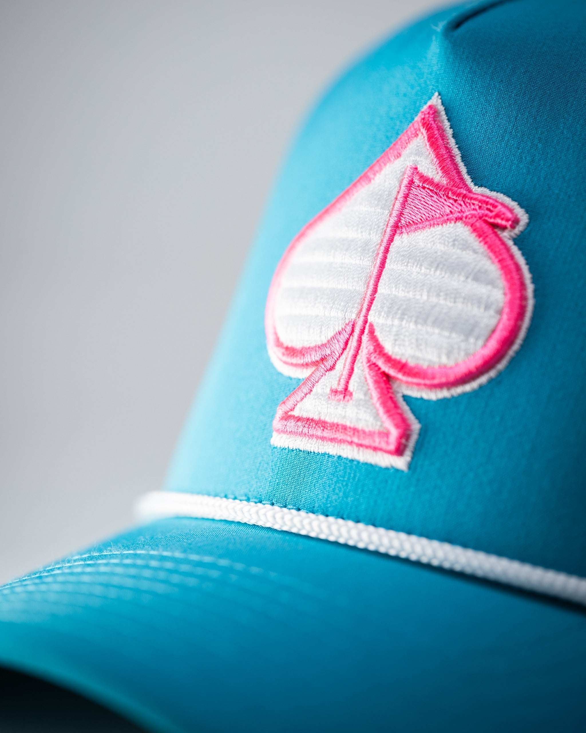 Baby blue perforated rope hat featuring a bold pink spade logo, perfect for stylish golfers on the course.